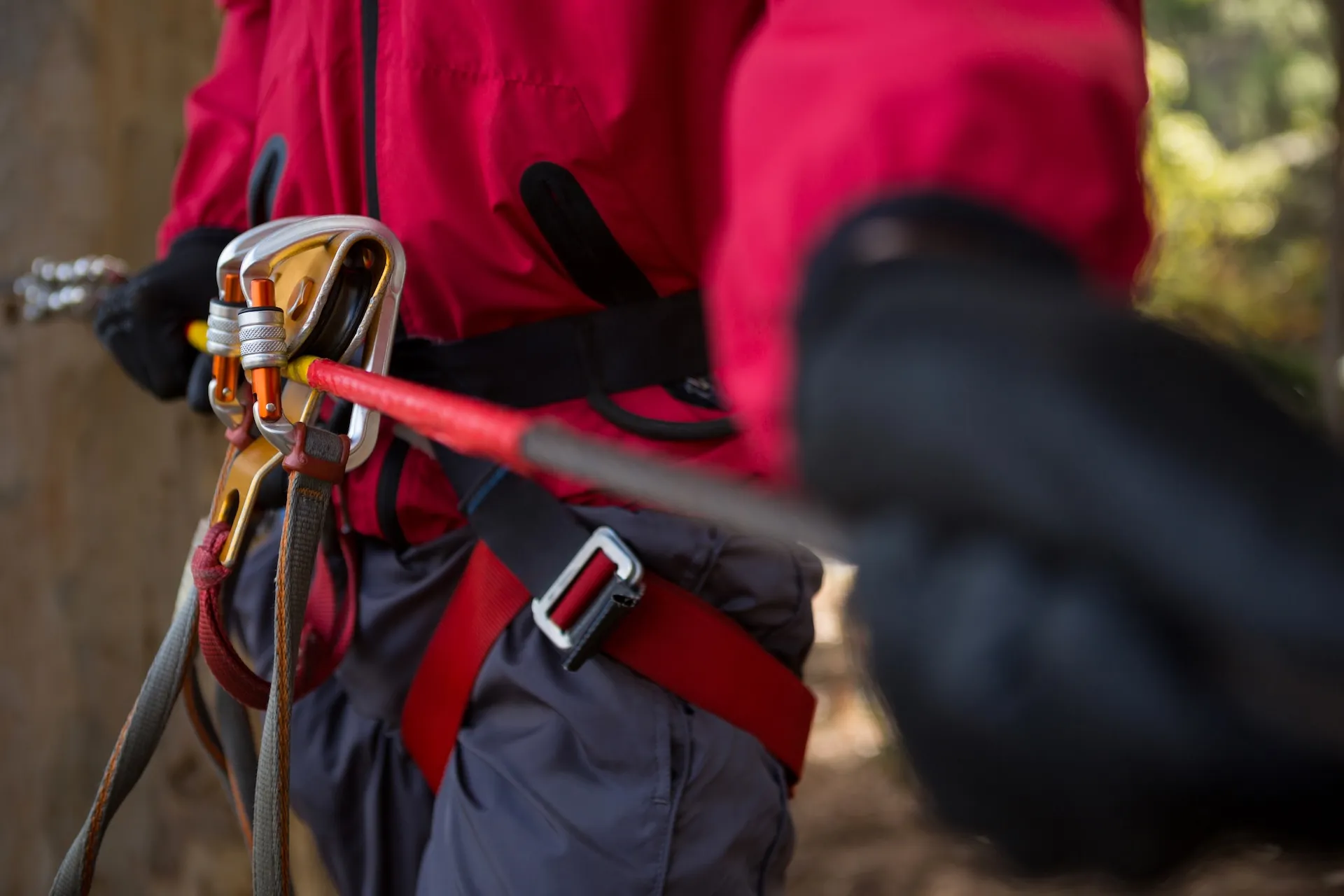 Person in a red jacket and harness clipped to a zip line in the forest
