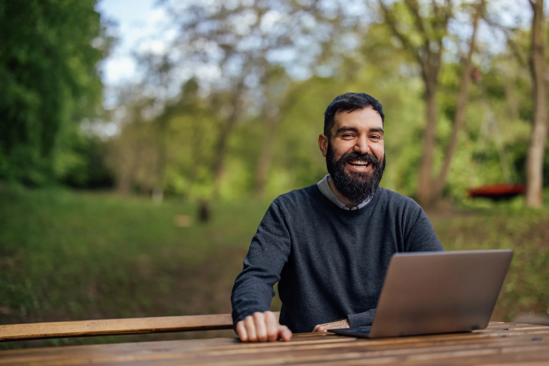 Smiling man working on a laptop at an outdoor picnic table
