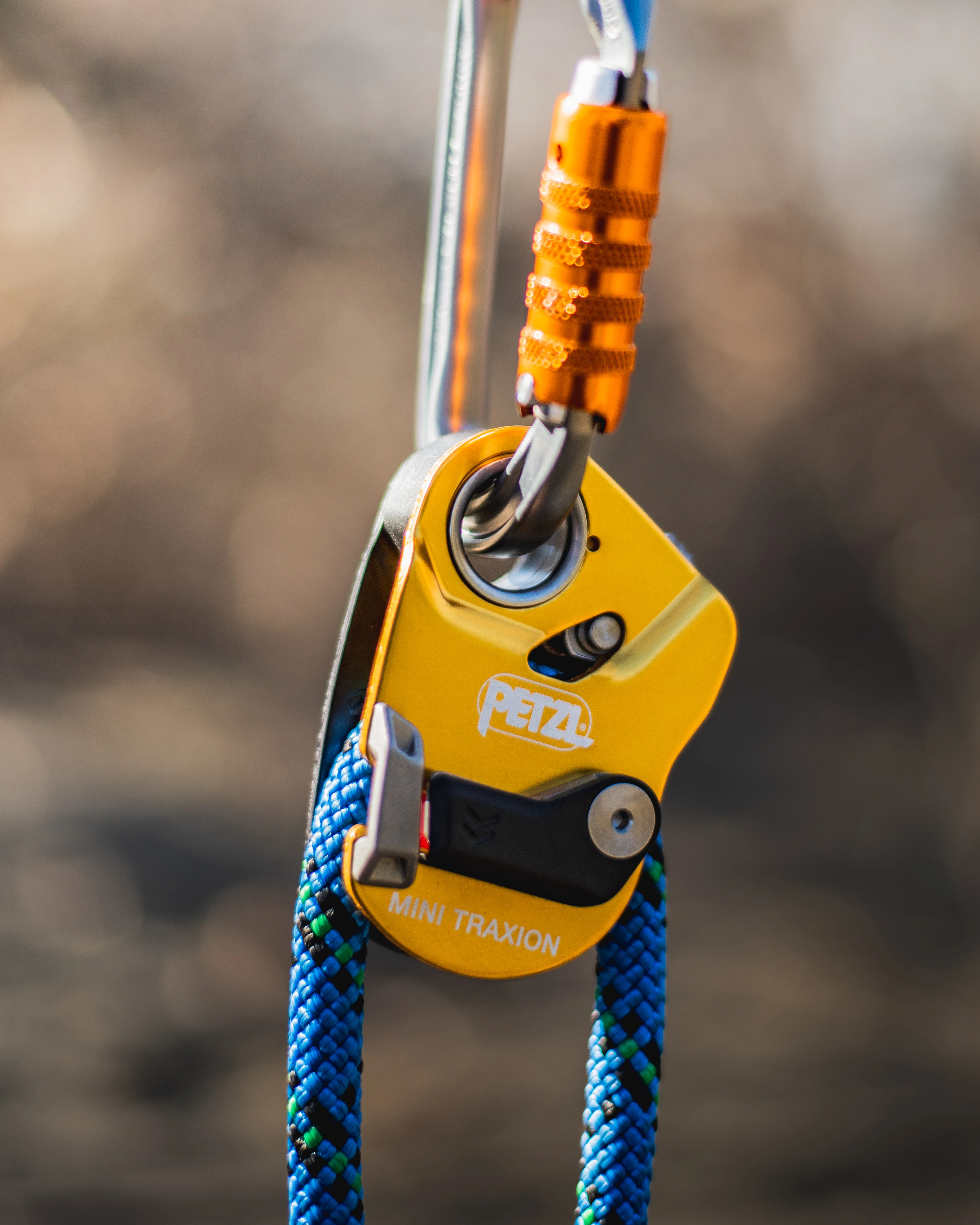 Yellow Petzl Mini Traxion pulley on blue rope hanging from an orange carabiner