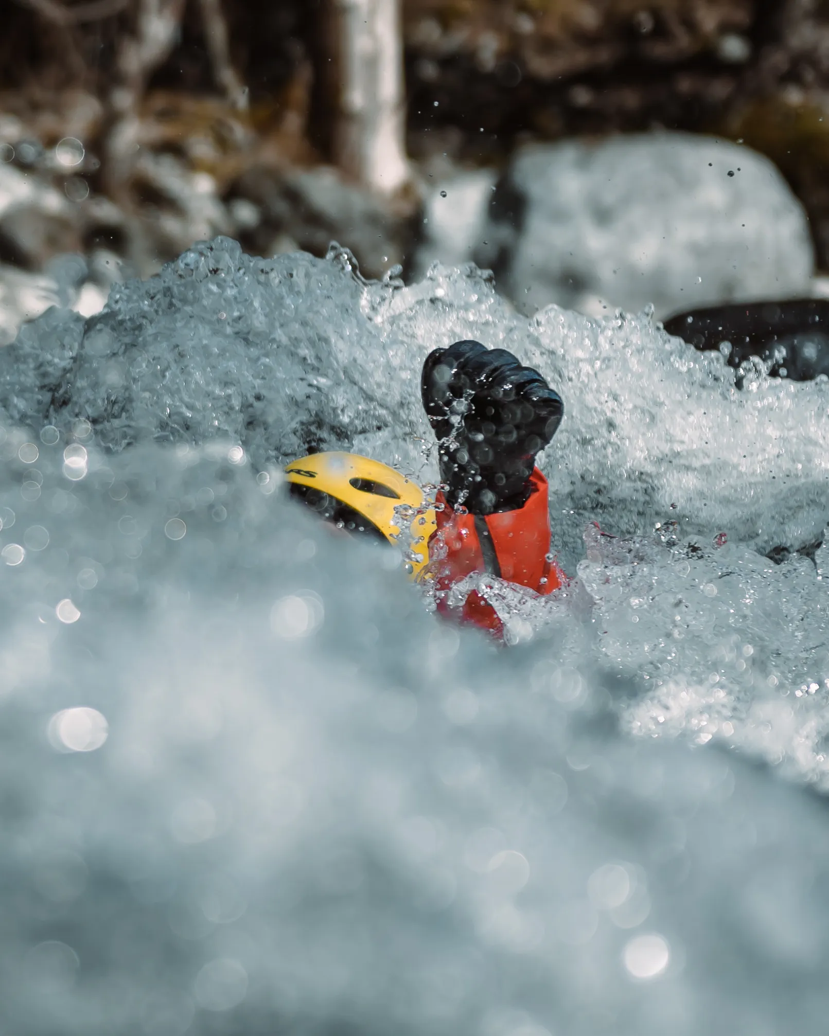 Rescue swimmer in a yellow helmet raising a gloved fist above whitewater