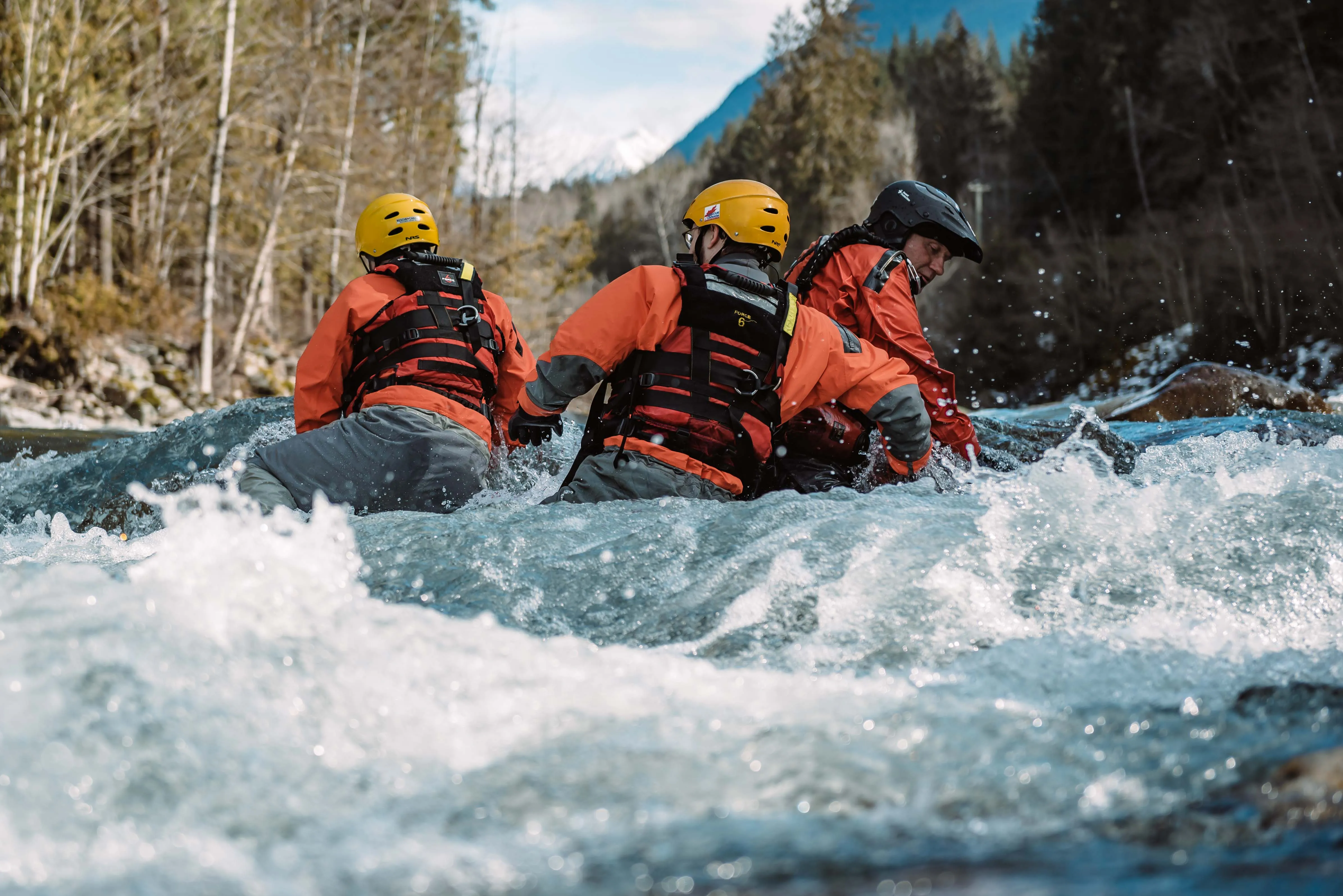 Three swiftwater rescue students in helmets and orange drysuits moving through whitewater together