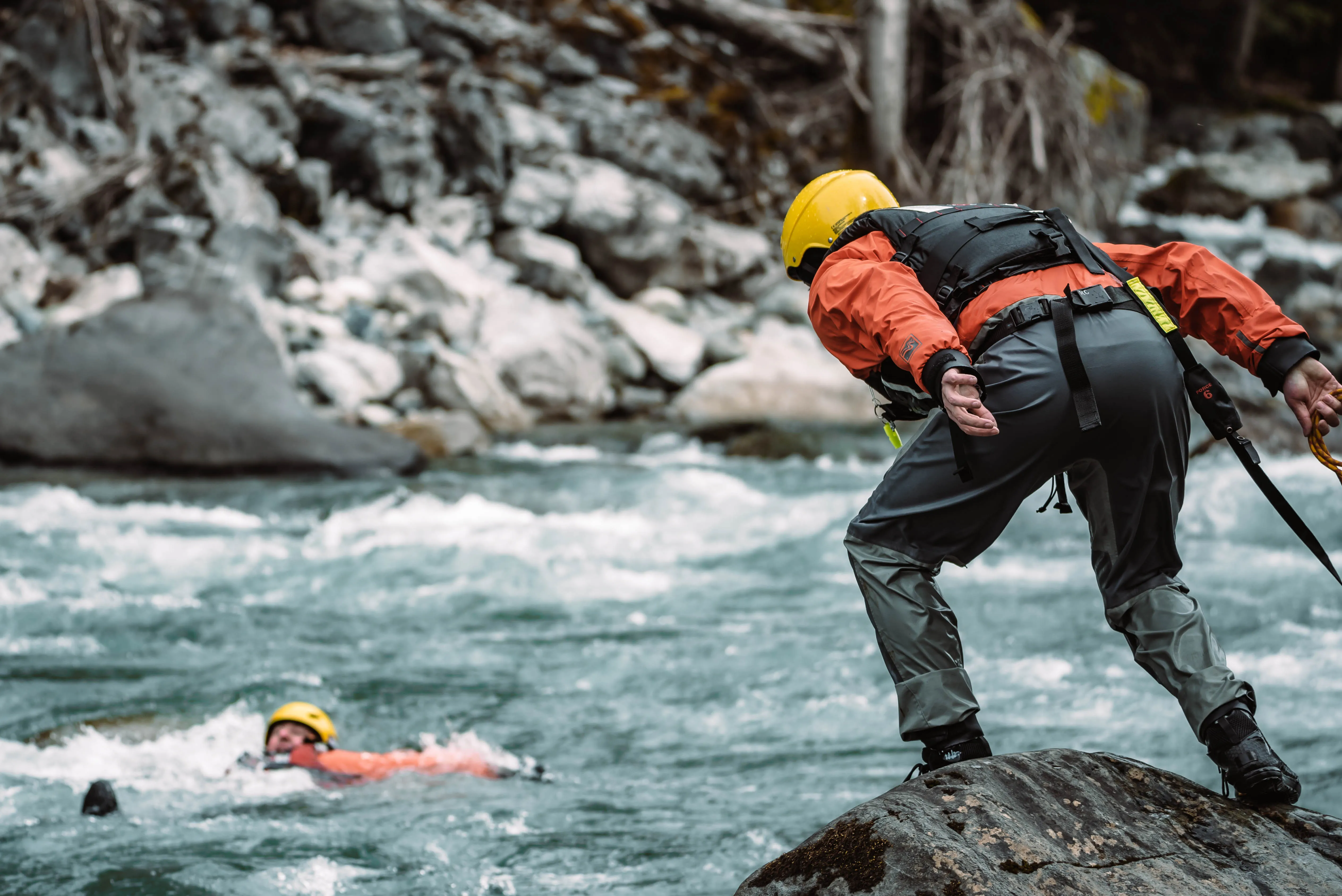 Rescuer on a boulder about to throw a rope to a swimmer in the river rapids