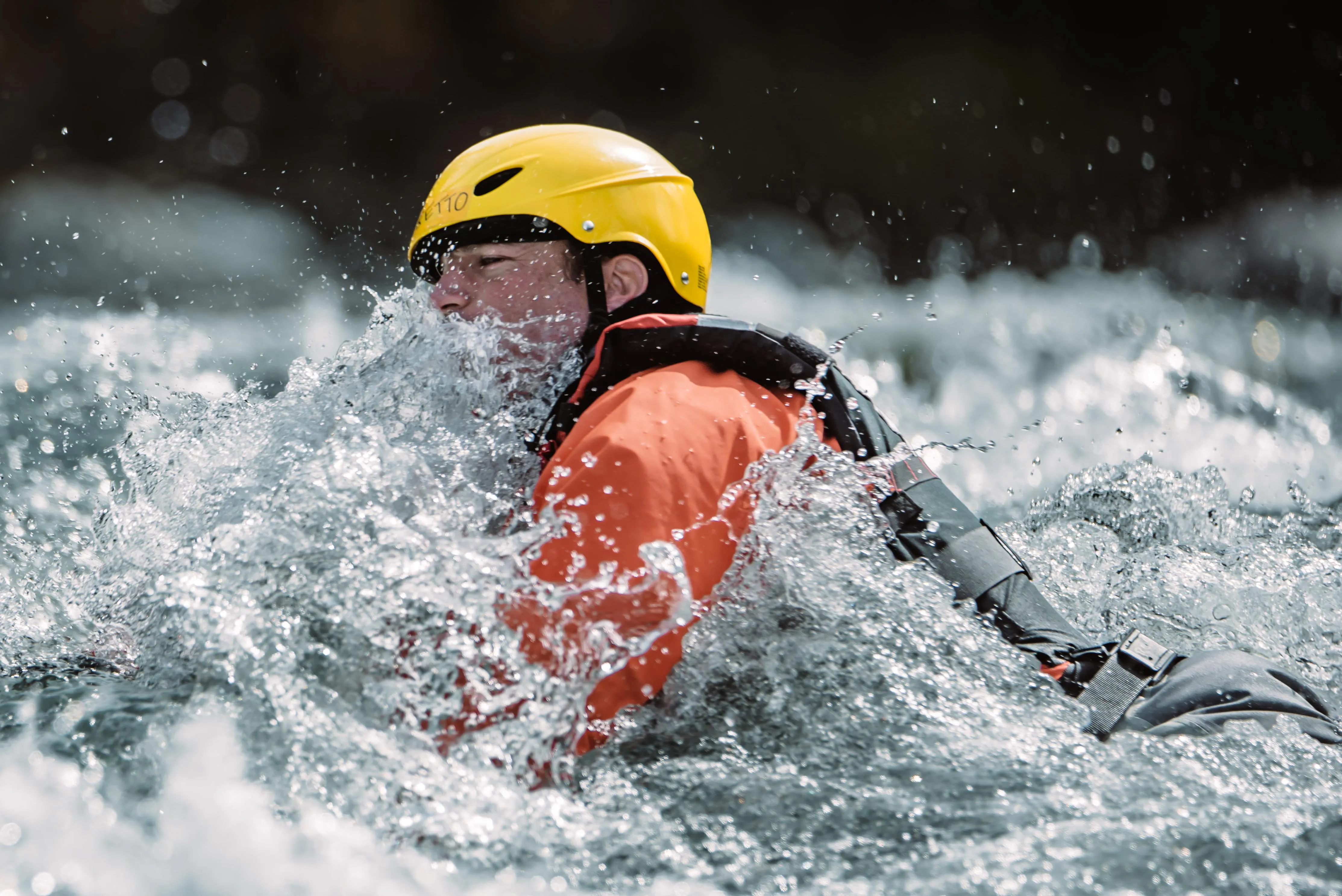 Rescue swimmer in a yellow helmet and orange drysuit pushing through whitewater