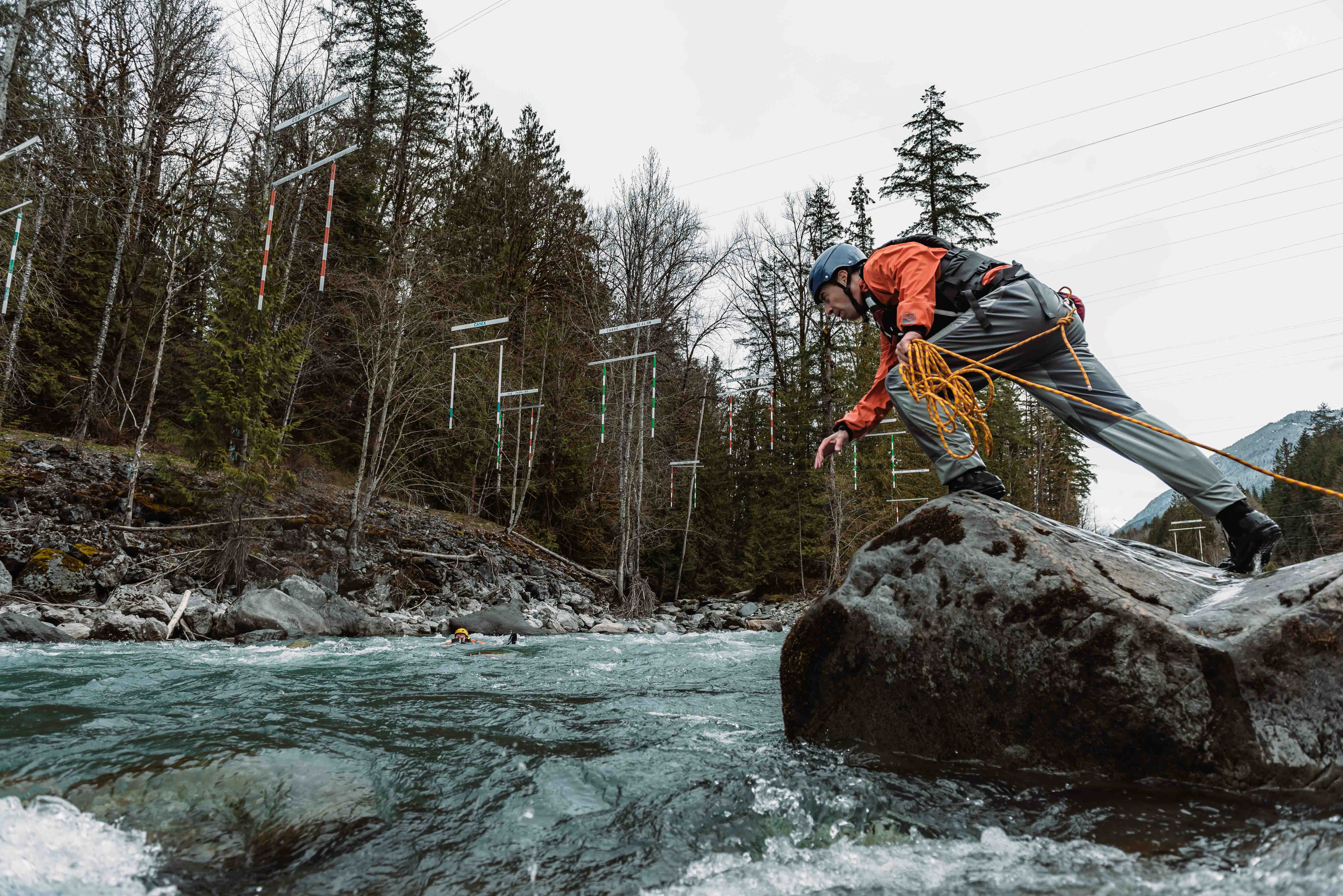 Swiftwater rescue student in a helmet and drysuit preparing to throw a rope from a boulder in a river