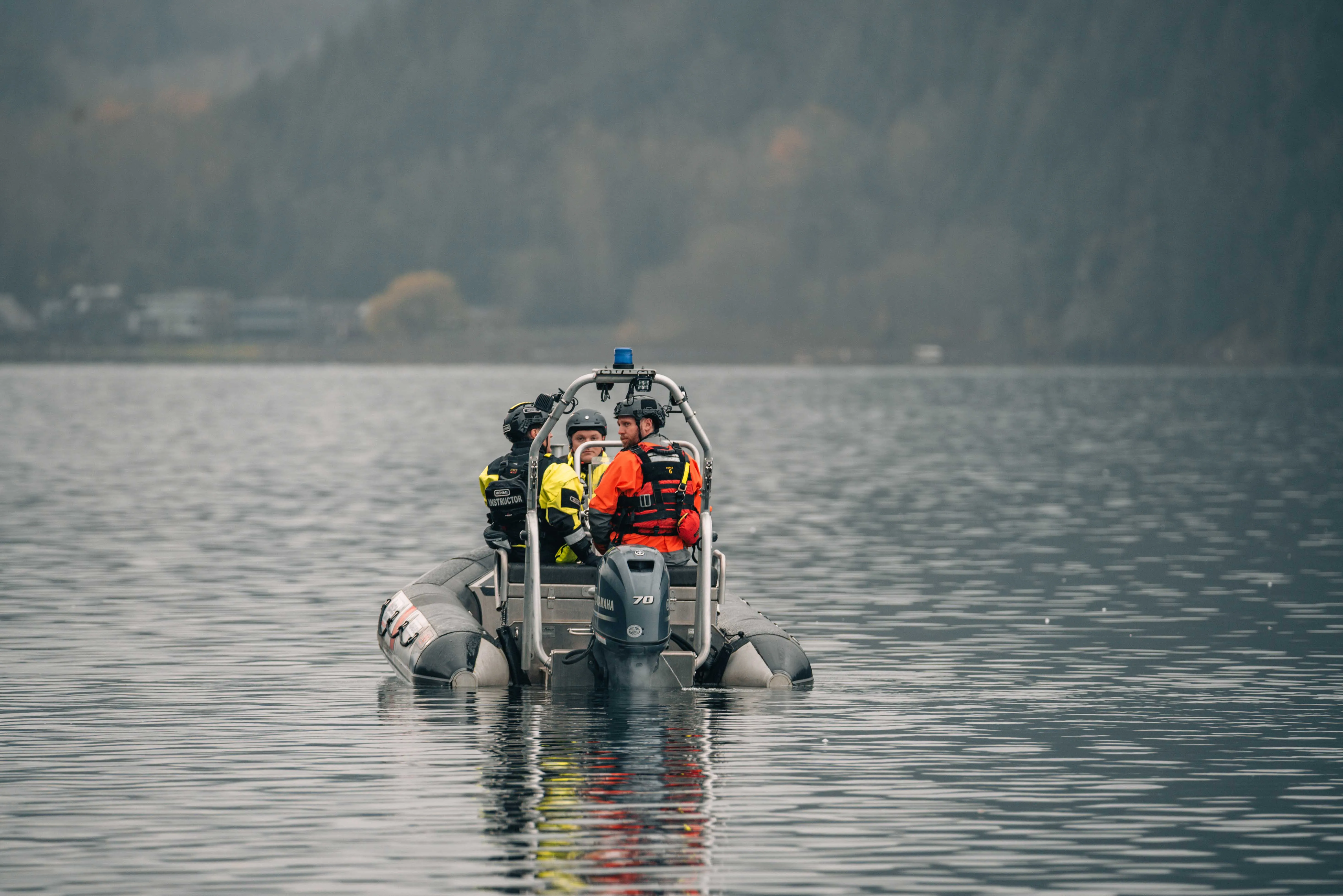 Rescue boat crew in drysuits and helmets on a calm misty lake
