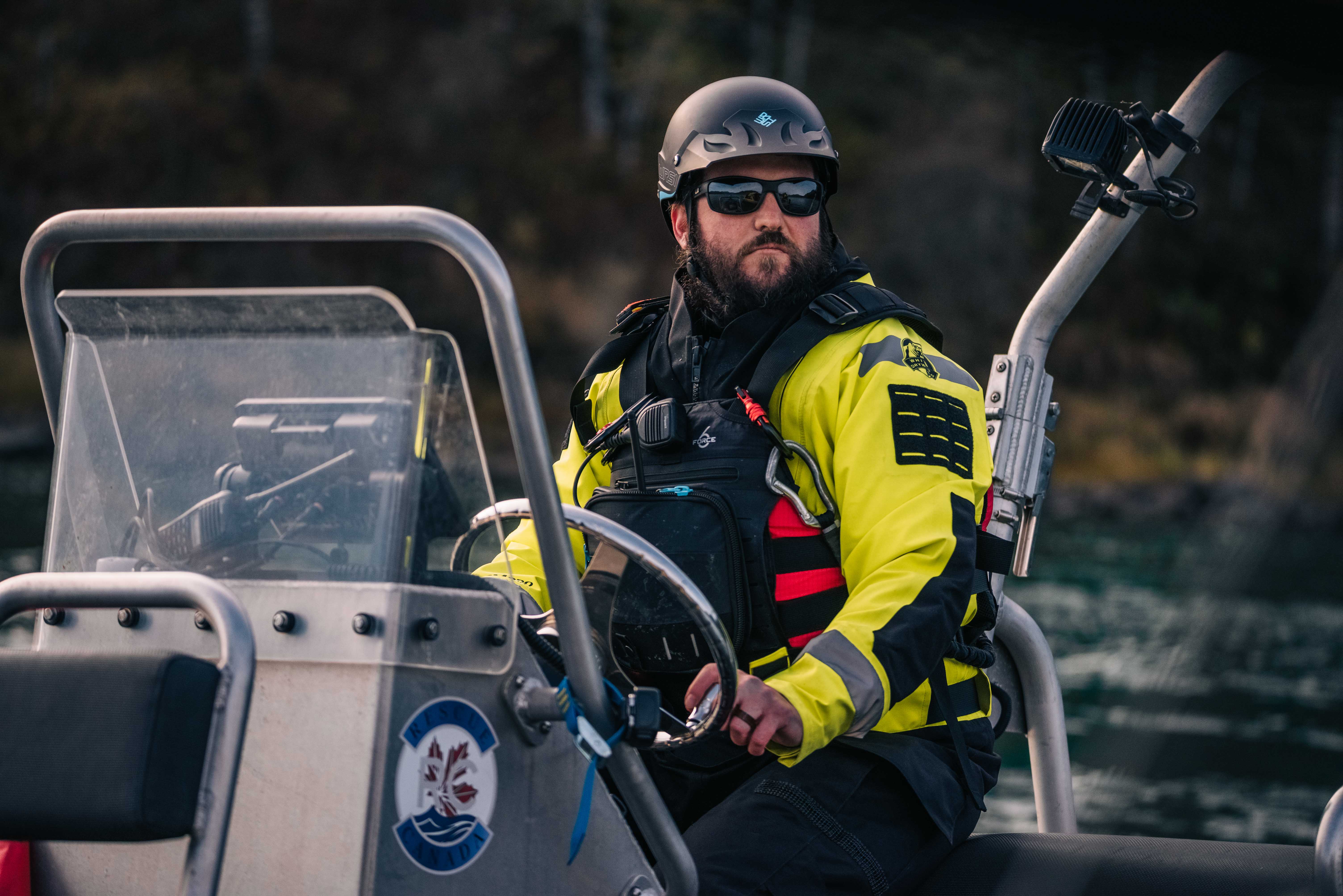 Boat operator in a helmet and yellow drysuit at the helm of a rescue boat