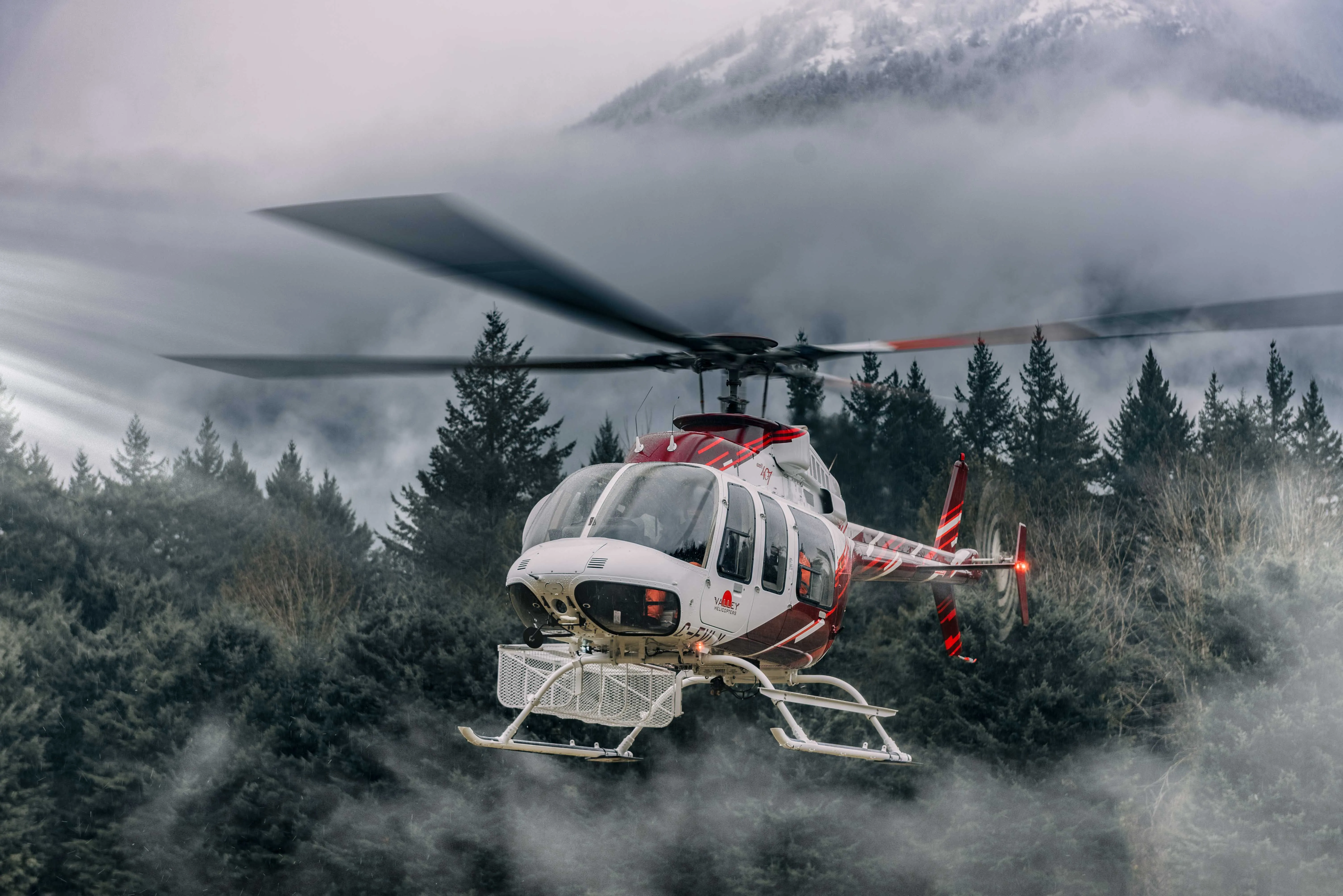 Red and white Bell helicopter lifting off in front of misty mountains