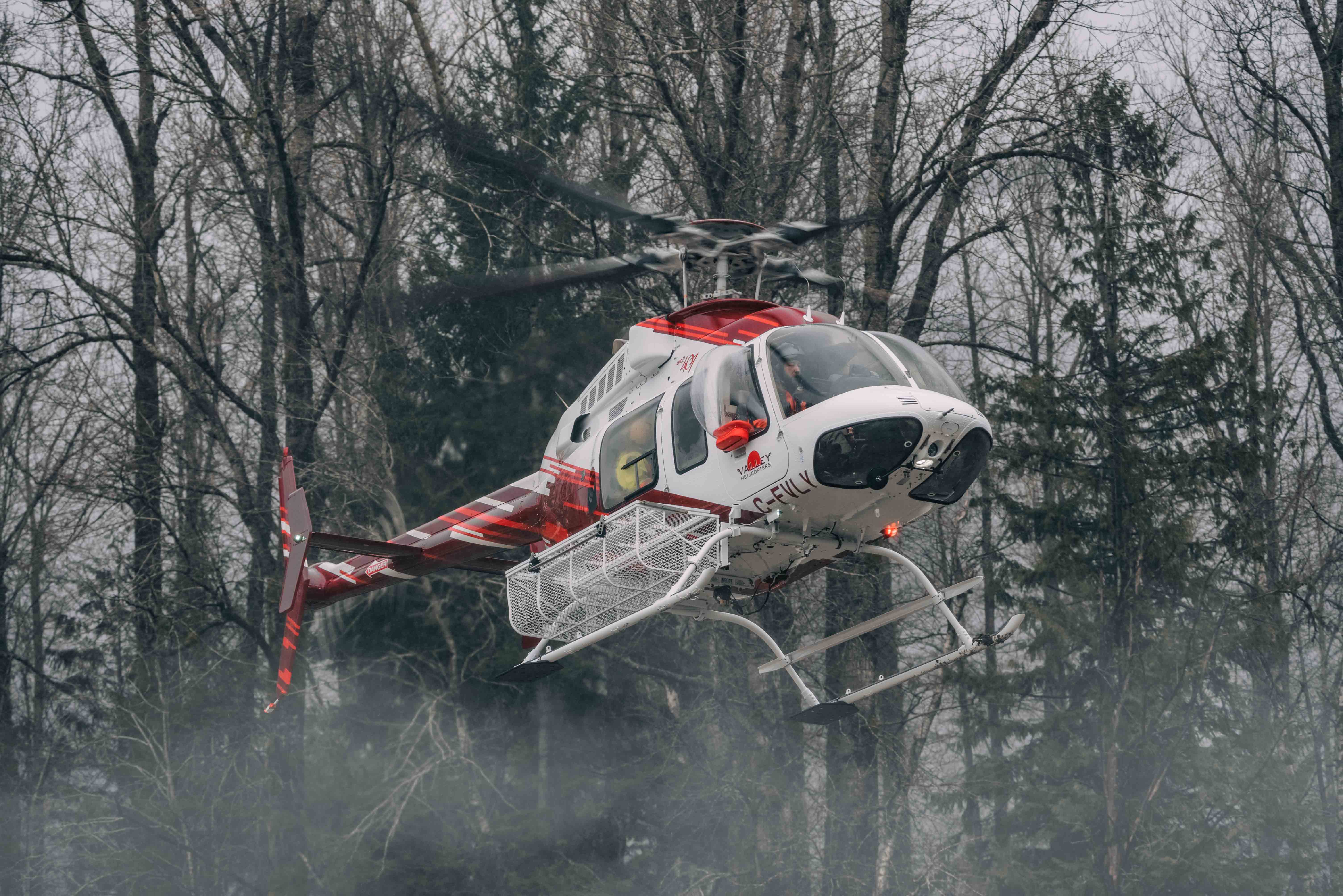 Red and white rescue helicopter hovering low over misty forest