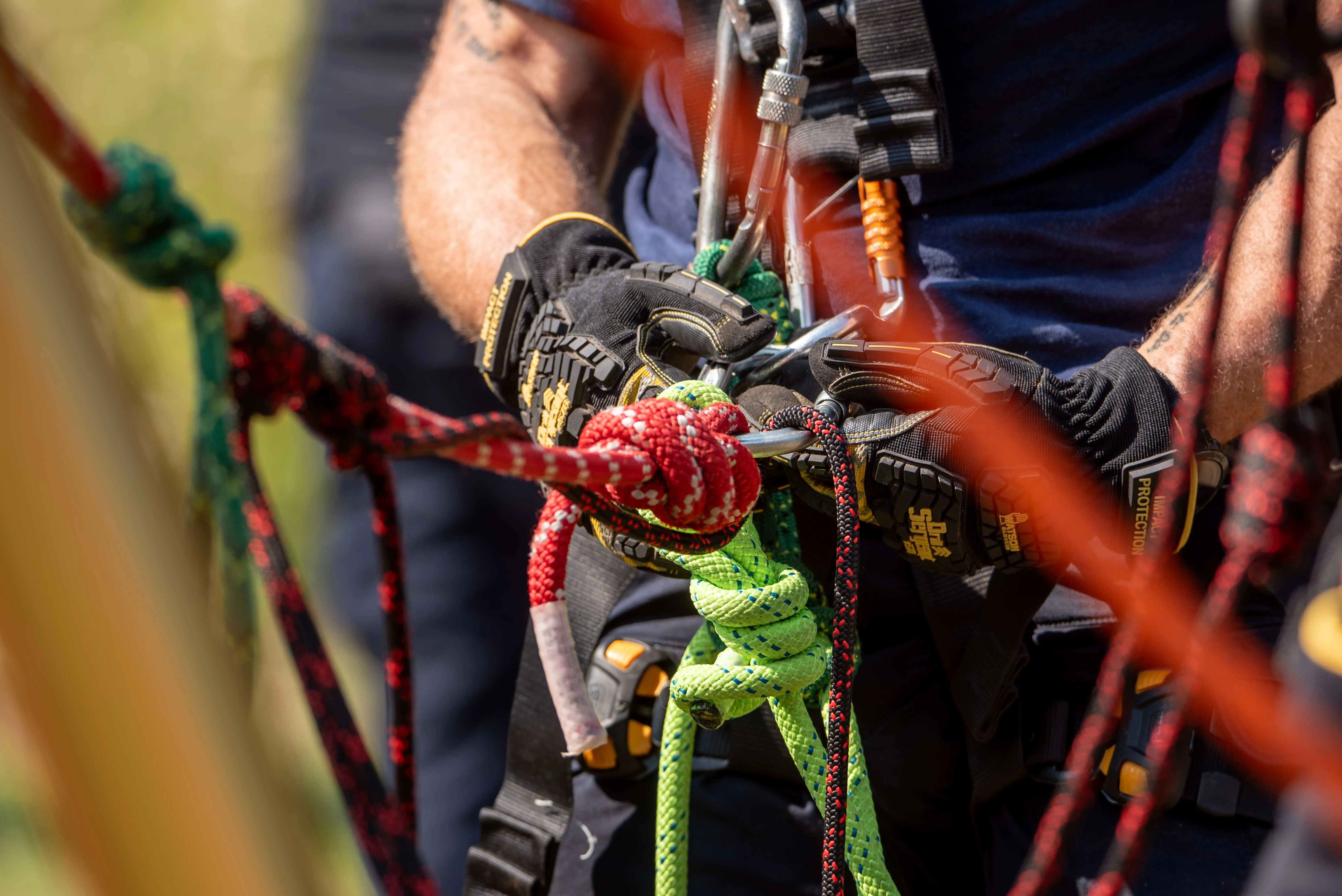 Gloved hands connecting red and green rescue ropes during rope rescue training