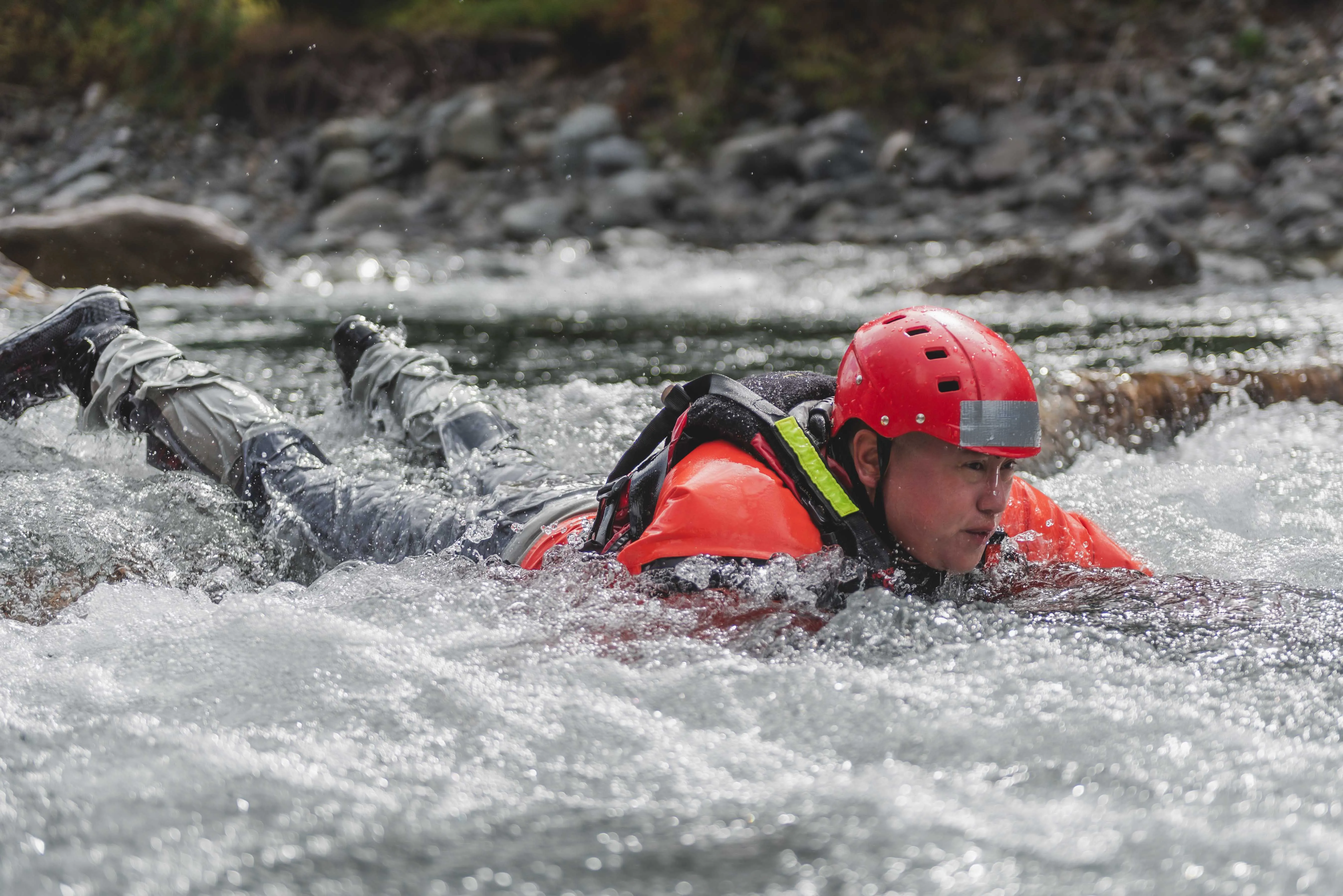 Swiftwater rescue student in a red helmet and PFD swimming aggressively through rapids