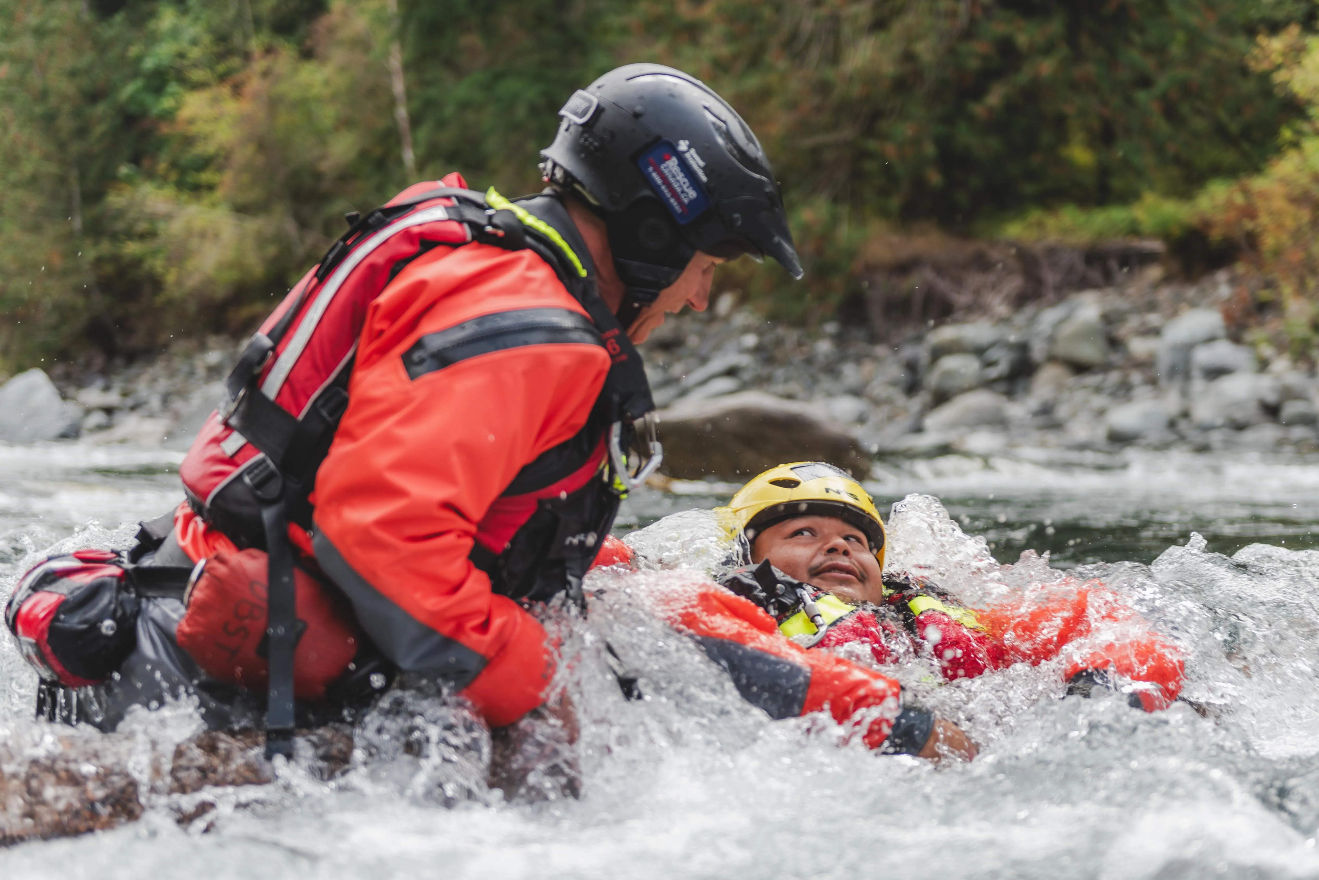 Swiftwater rescue technician holding a swimmer in a yellow helmet steady in river rapids