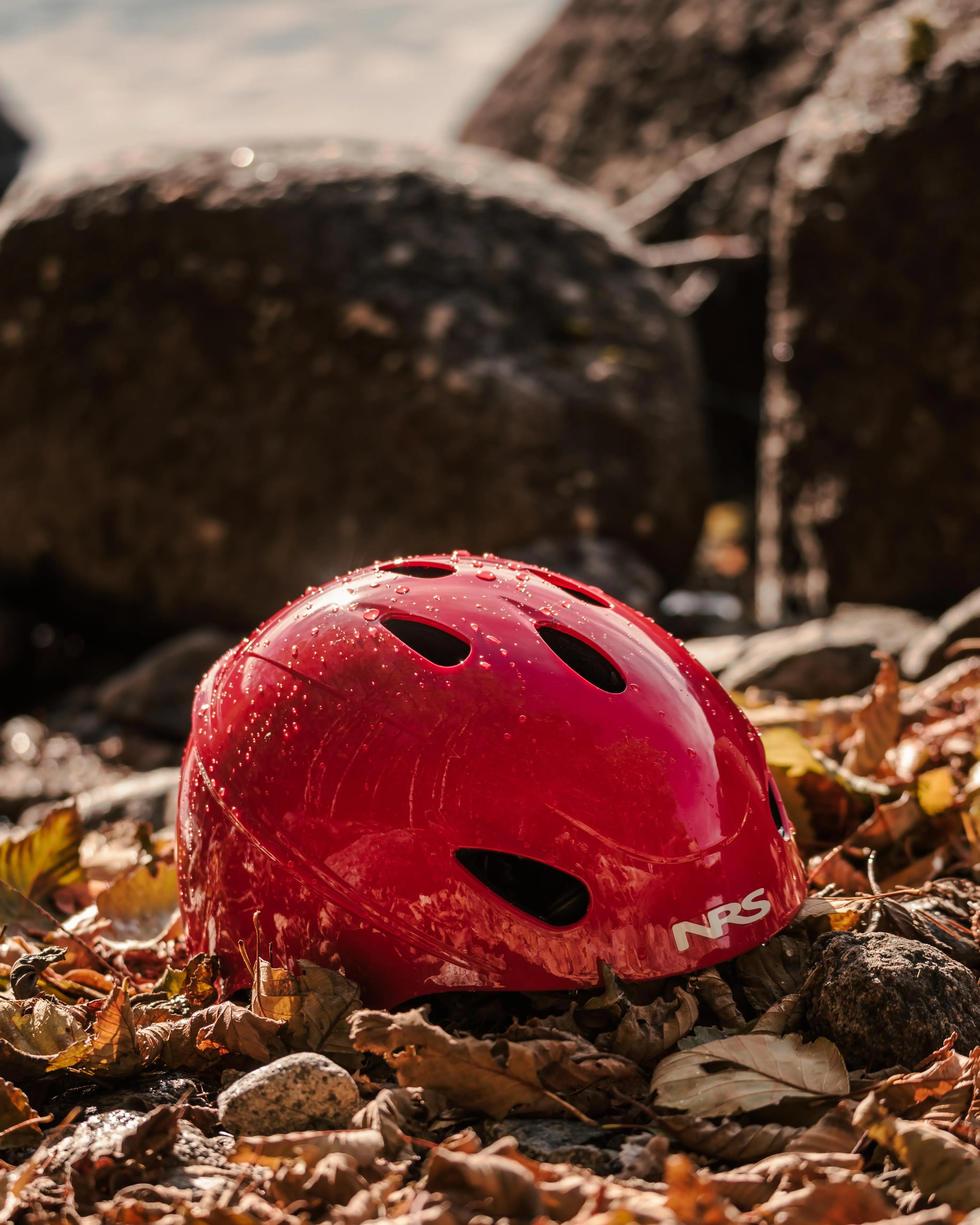 Red NRS water rescue helmet resting on autumn leaves by the shore
