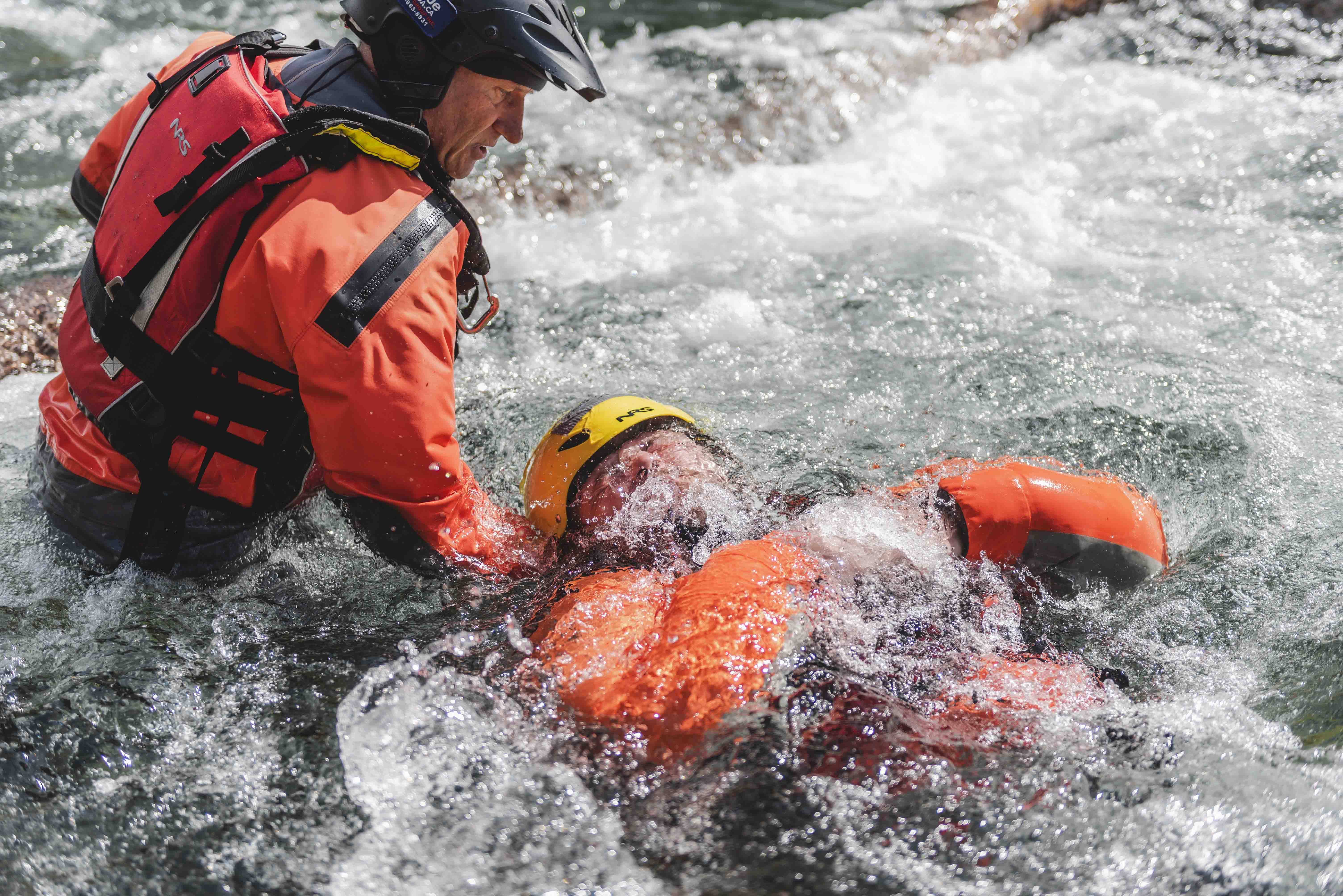 Swiftwater rescue technician pulling a swimmer in an orange drysuit through river rapids