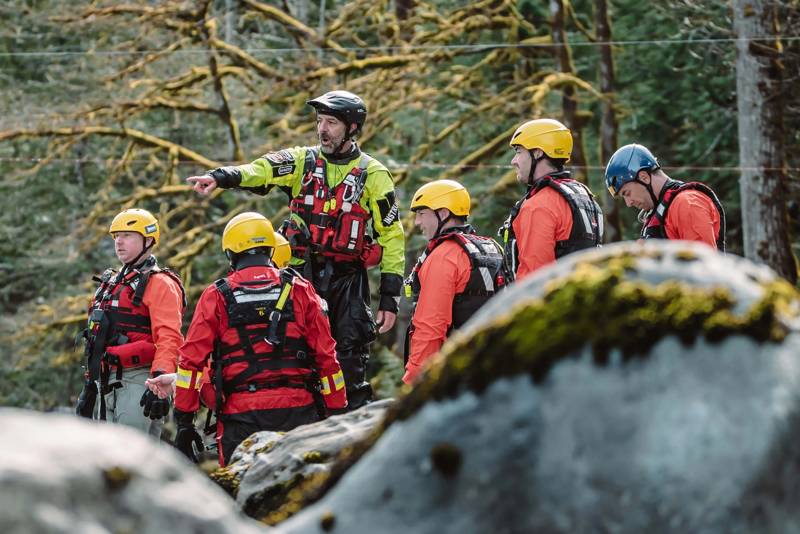 Instructor pointing out river hazards to a group of swiftwater rescue students in helmets and PFDs