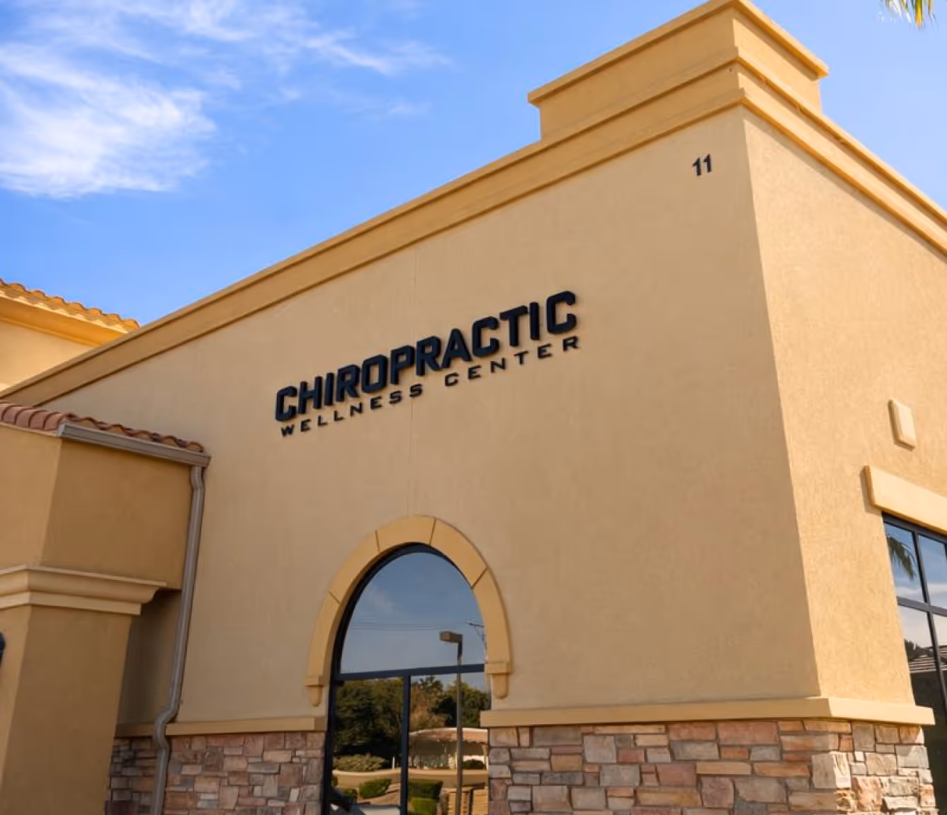 Exterior of a beige building with a sign reading Chiropractic Wellness Center under blue sky. Foresight Wellness Center exterior.