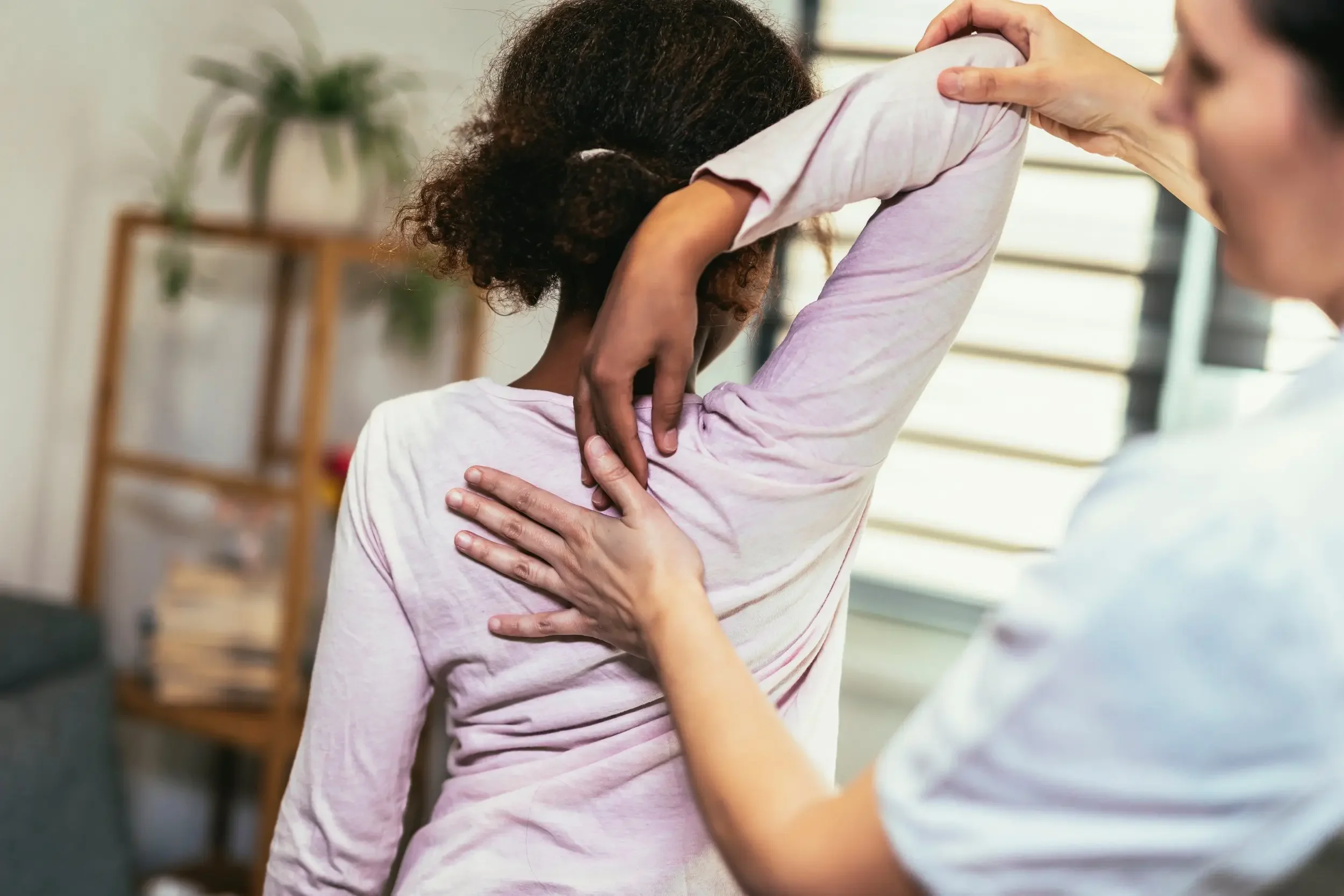 Chiropractor examining a child's upper back while helping stretch the child's arm.