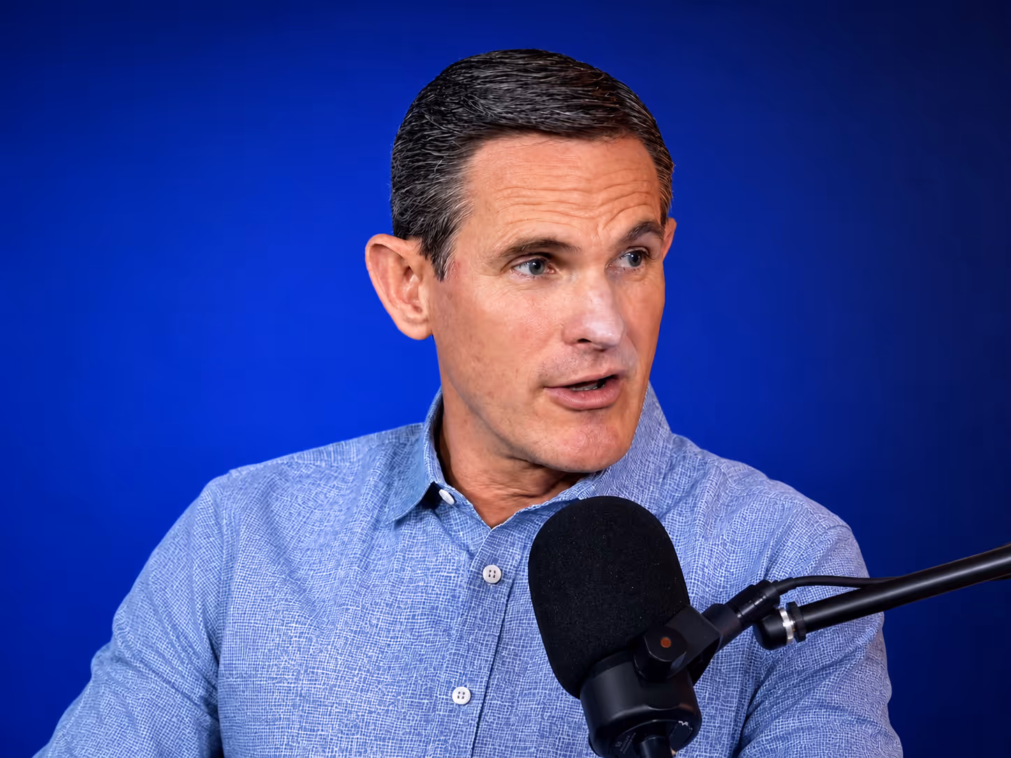 Dr. Keith Lavender with dark hair speaking into a black microphone against a blue background.