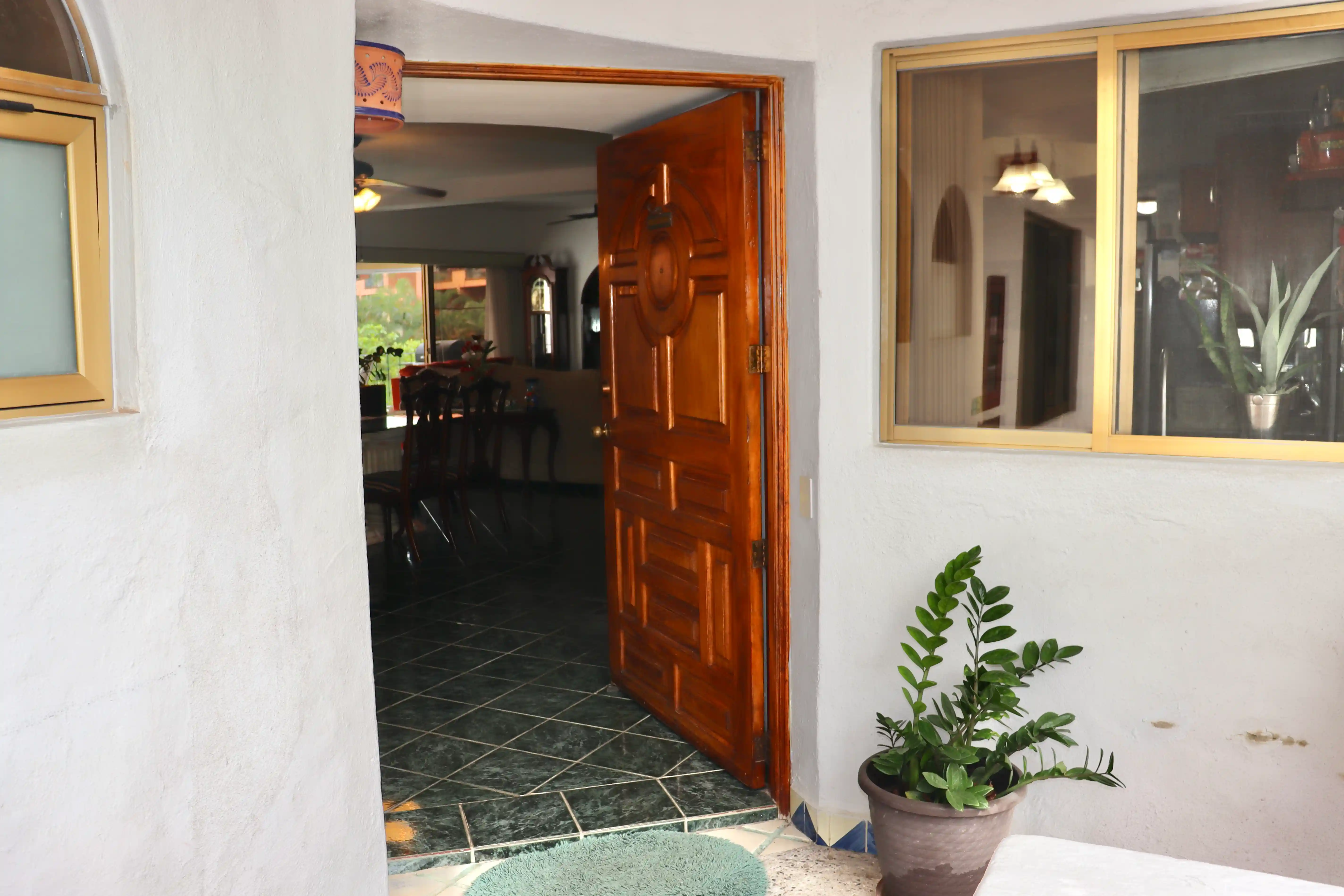 Main entrance of Royal Pacific 2304 in Marina Vallarta, featuring a classic solid wood door opening into a bright, spacious living area with traditional Mexican architectural charm and polished floors.