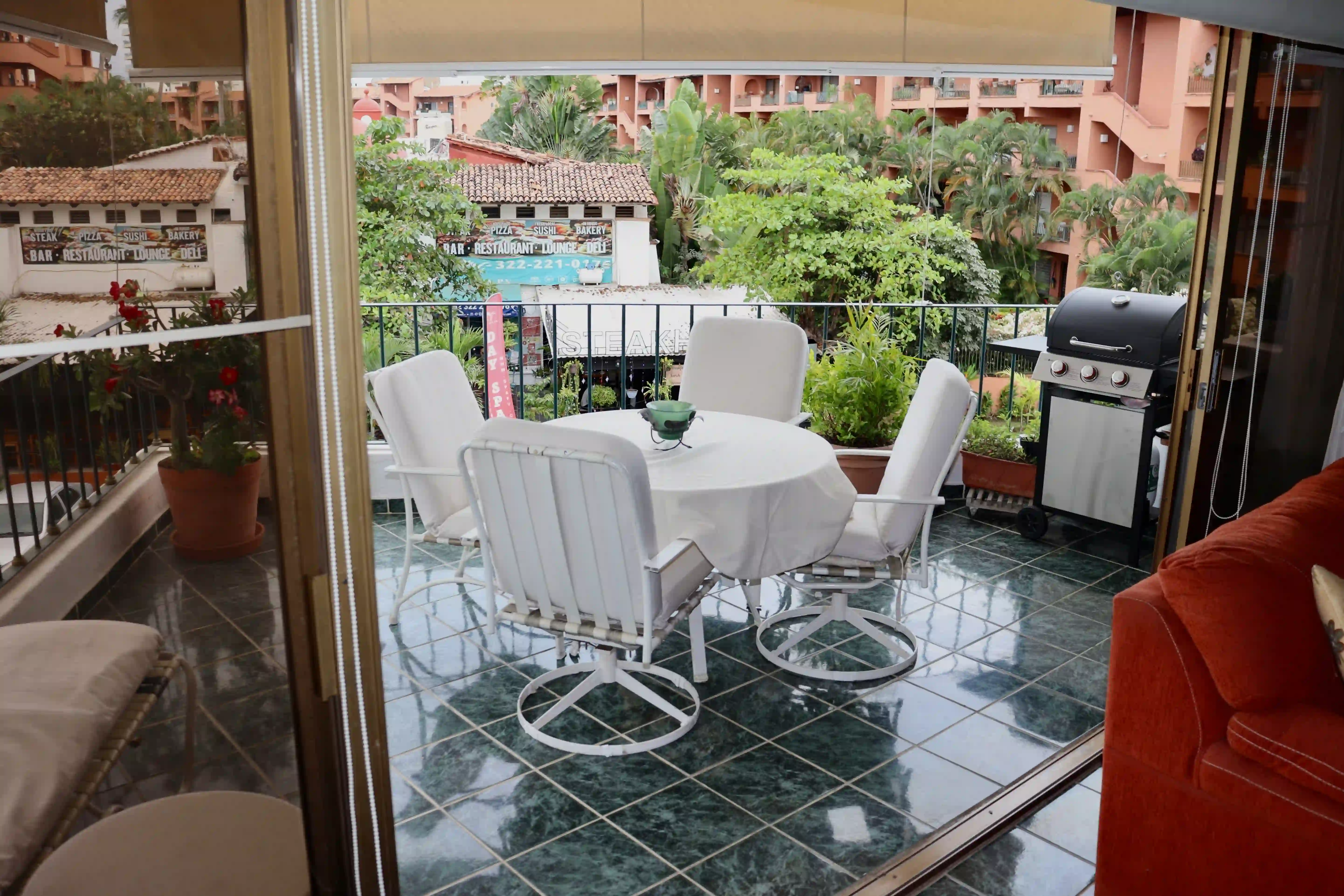 Private covered balcony at Royal Pacific with a classic white dining set, overlooking lush tropical gardens and the pool area of the development.