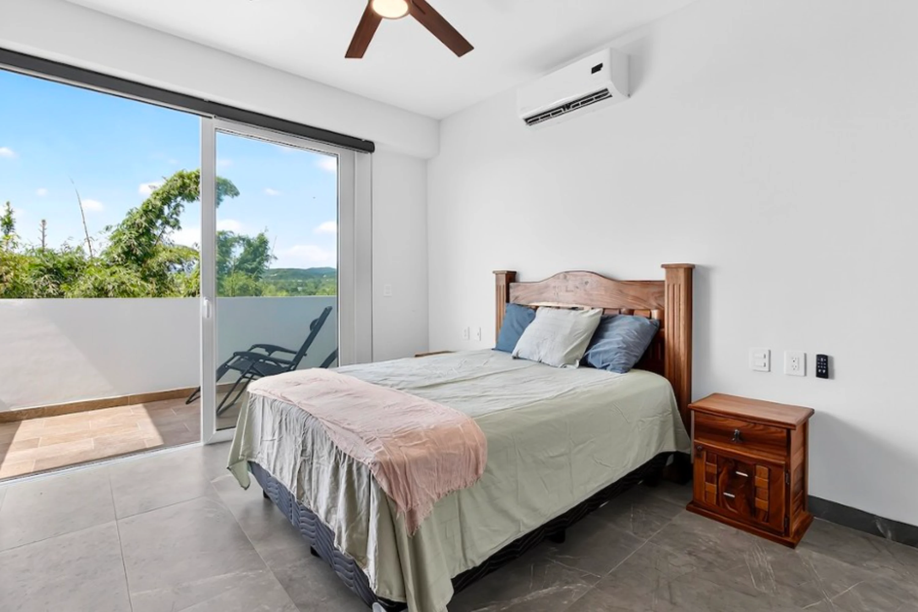 Master bedroom with a minimalist aesthetic, featuring a large bed, neutral decor, and direct access to a balcony with scenic views.
