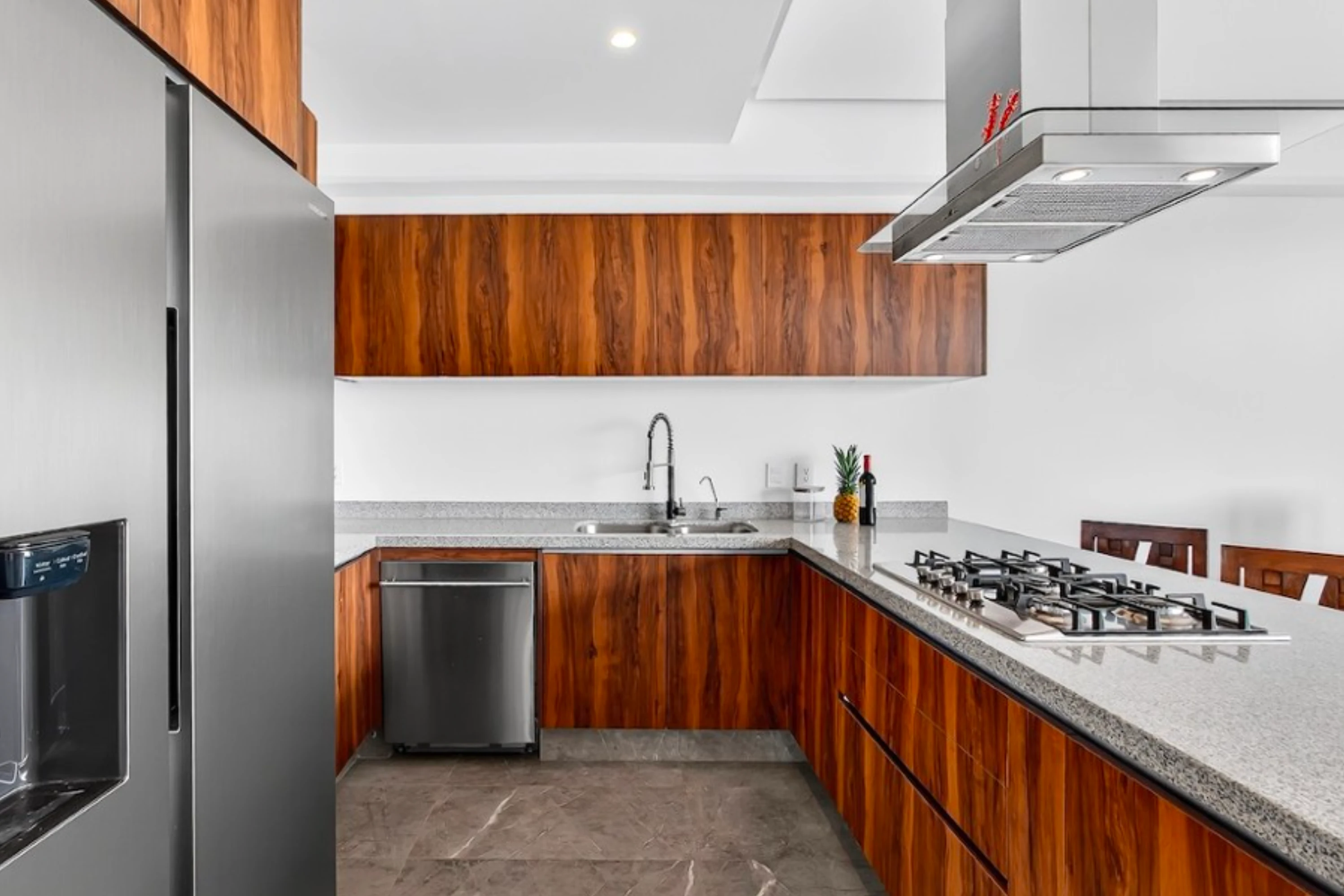 Sleek modern kitchen featuring a marble-style breakfast bar, minimalist white cabinetry, and high-end stainless steel appliances.