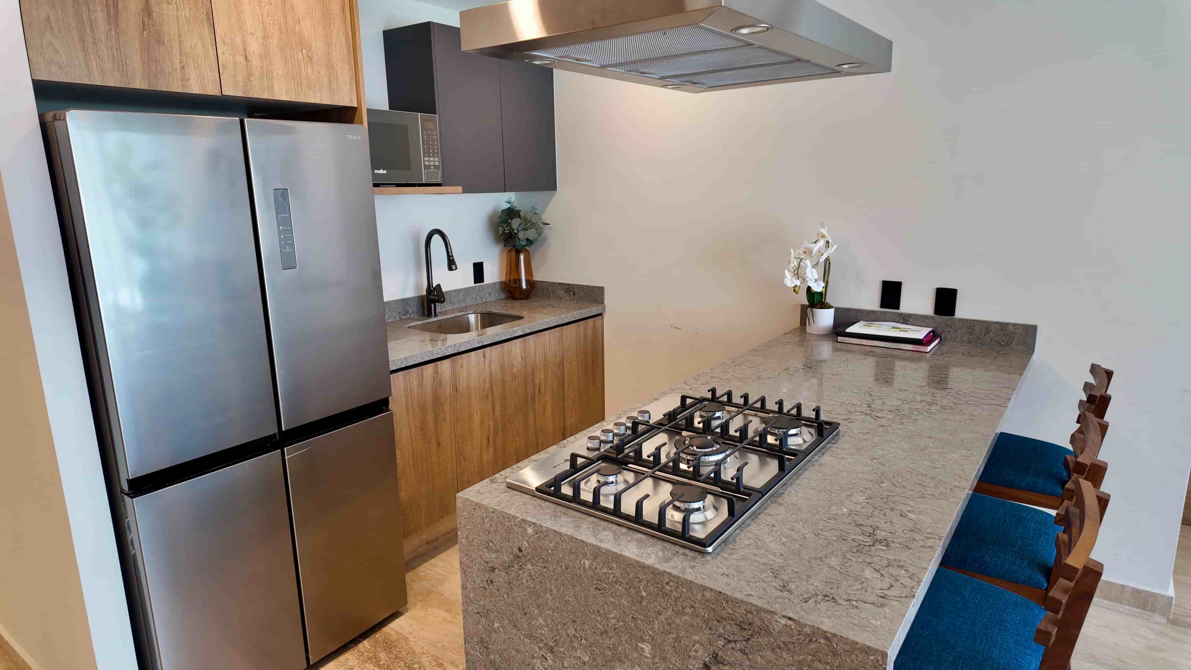 Modern kitchen workspace featuring stainless steel appliances, premium wooden cabinetry, and an elegant breakfast bar stool setup.