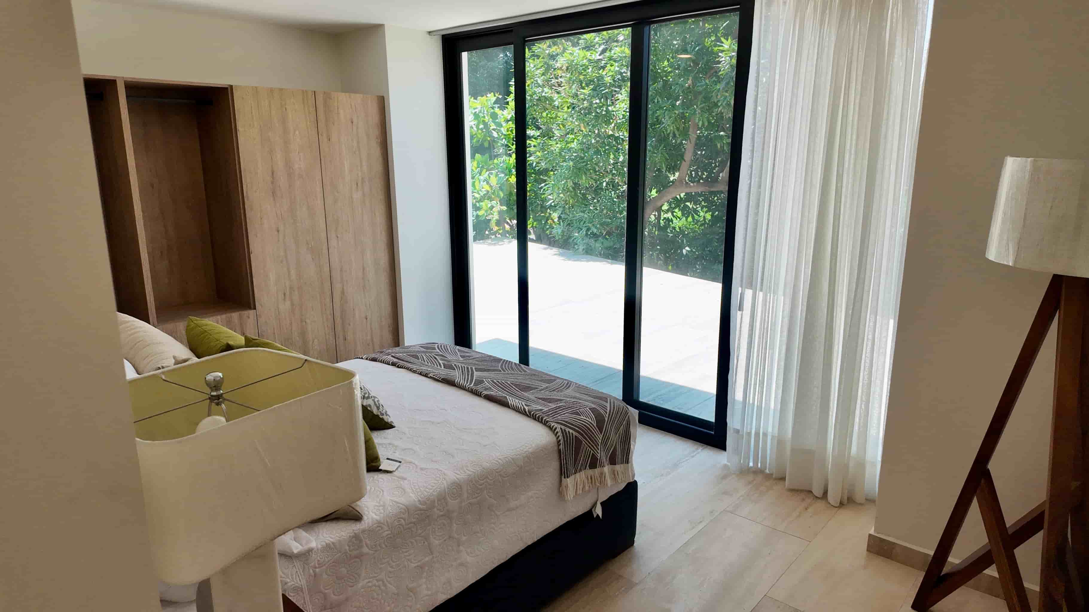 Spacious guest bedroom layout featuring a plush bed, built-in wooden closet, and large glass sliding doors to the exterior.