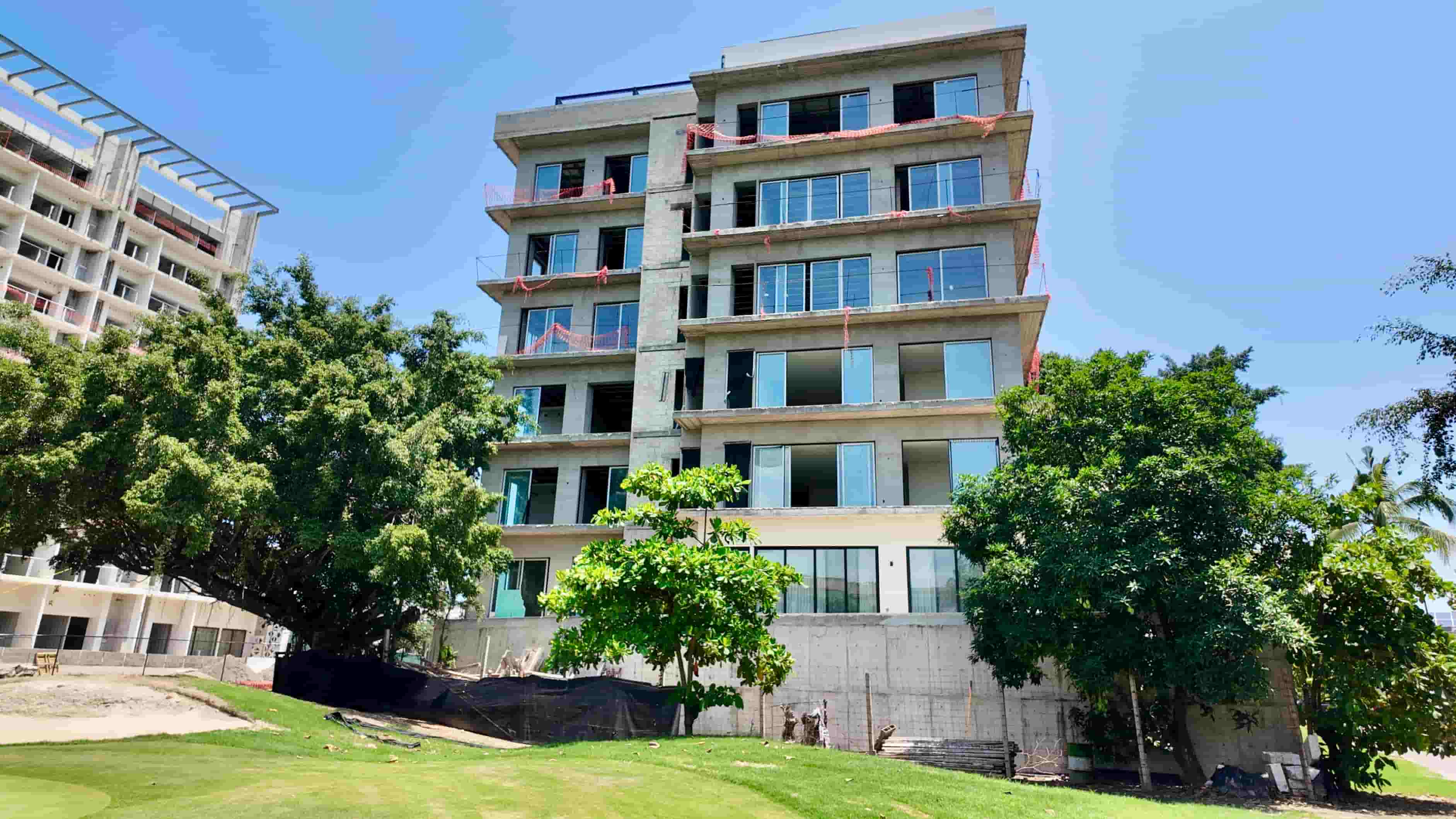 Real exterior photograph of the Batros building structure under a clear blue sky, surrounded by green trees in Puerto Vallarta.