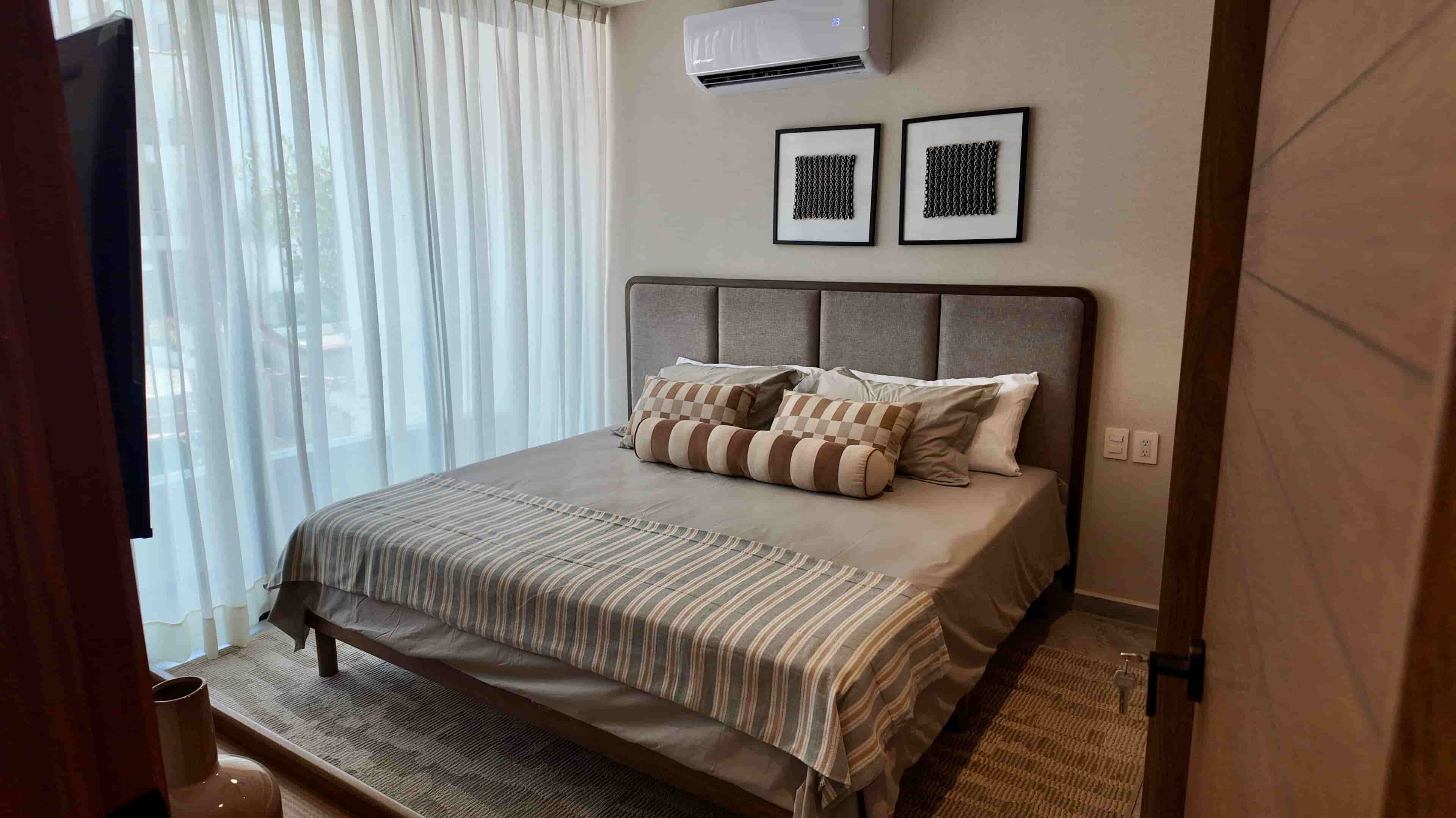 Master bedroom with a large bed, custom wooden headboard, and neutral-colored linens in the TERRA 242 model apartment.