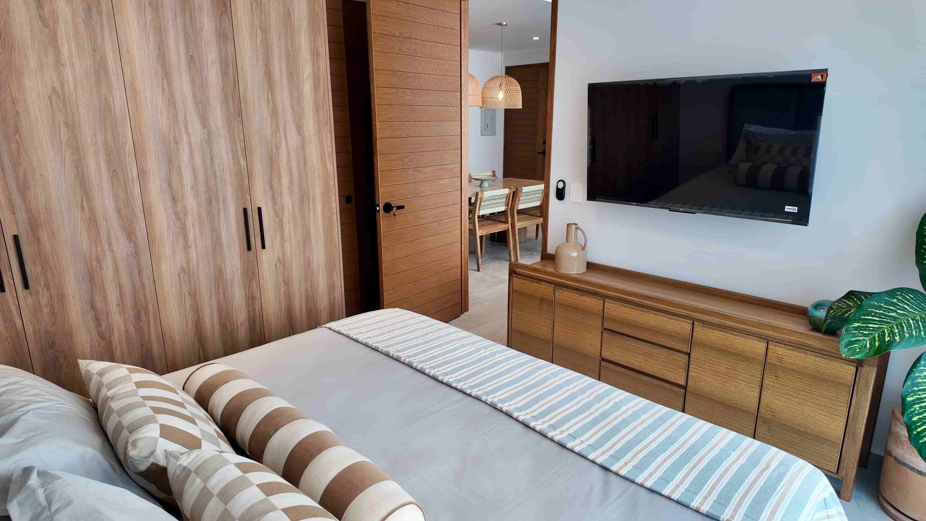Bright bedroom interior showing a modern wooden dresser, wall-mounted TV, and elegant accent decor inside TERRA 242.
