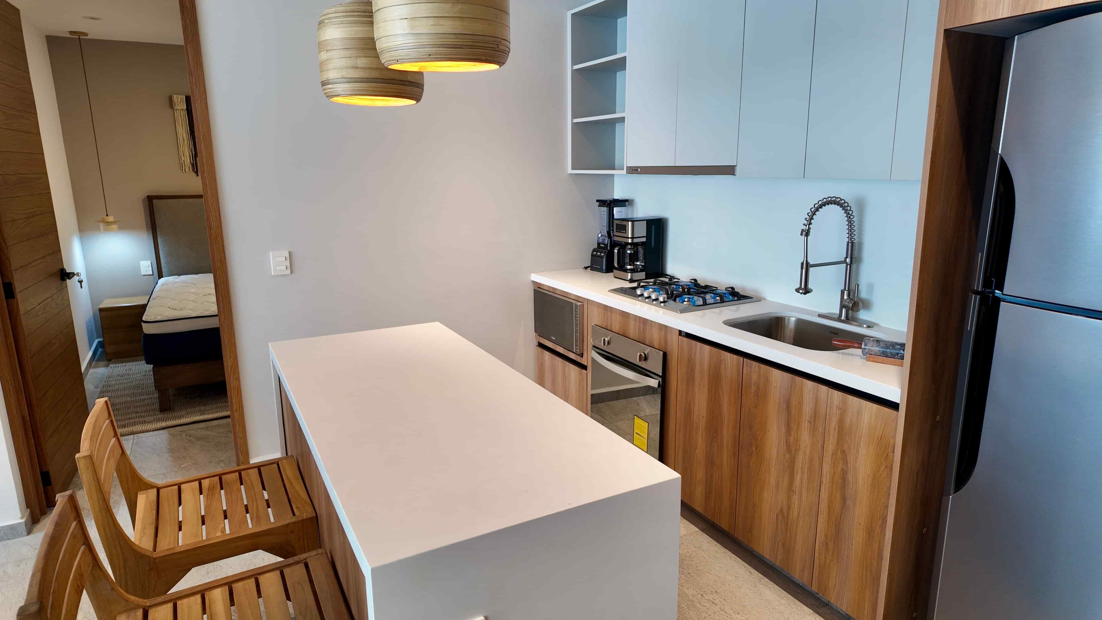 Functional kitchen design with a minimalist white quartz island and wooden breakfast bar stools in the TERRA 242 model unit.
