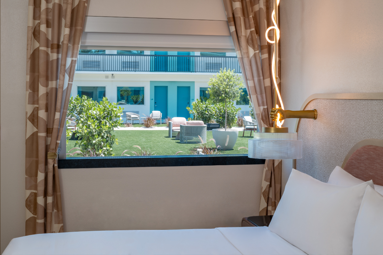 Hotel room with a bed near a window overlooking a courtyard with chairs and greenery.