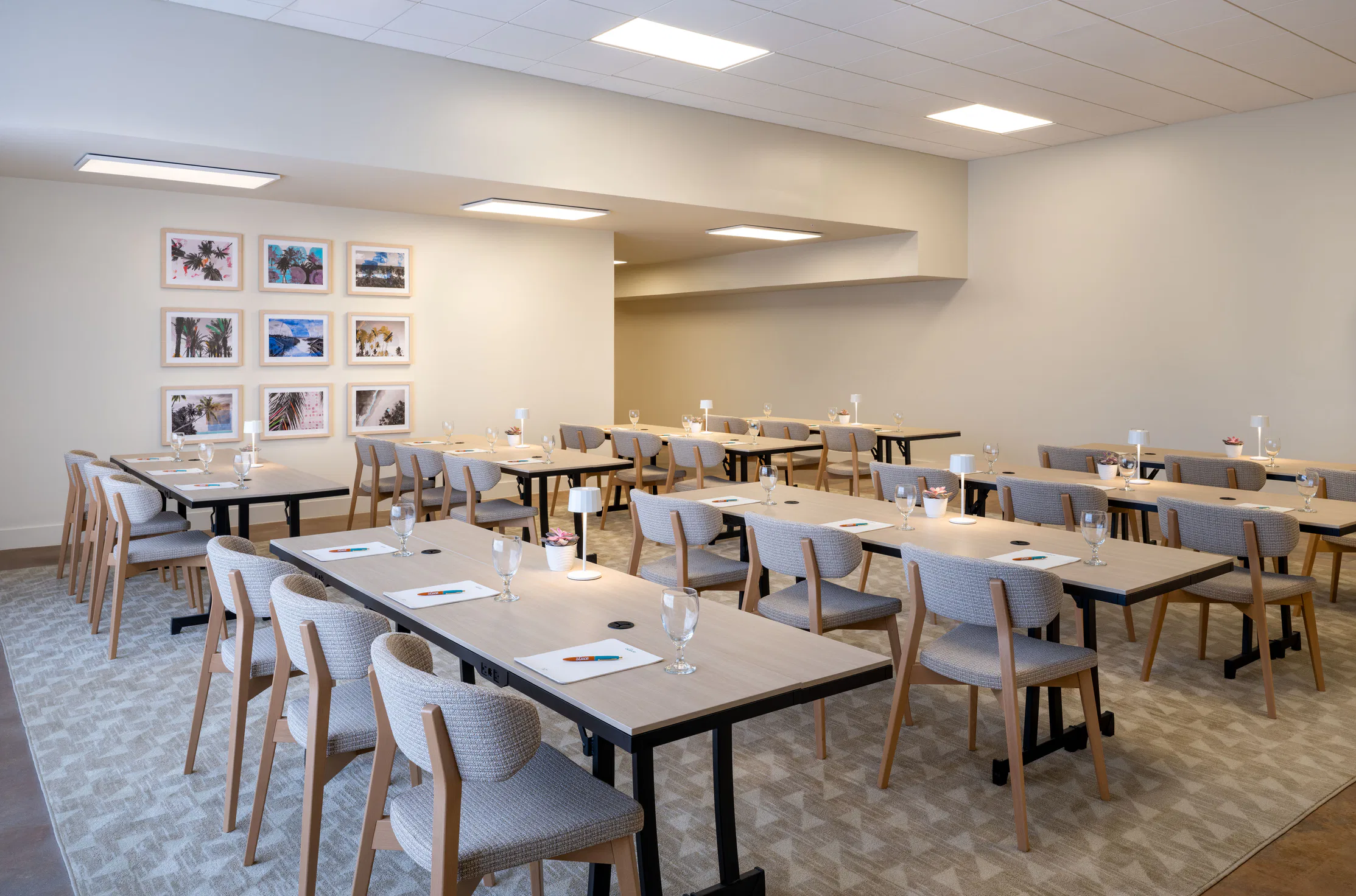 Modern conference room with wooden tables, grey chairs, notepads, pens, glasses, and wall art with photos.
