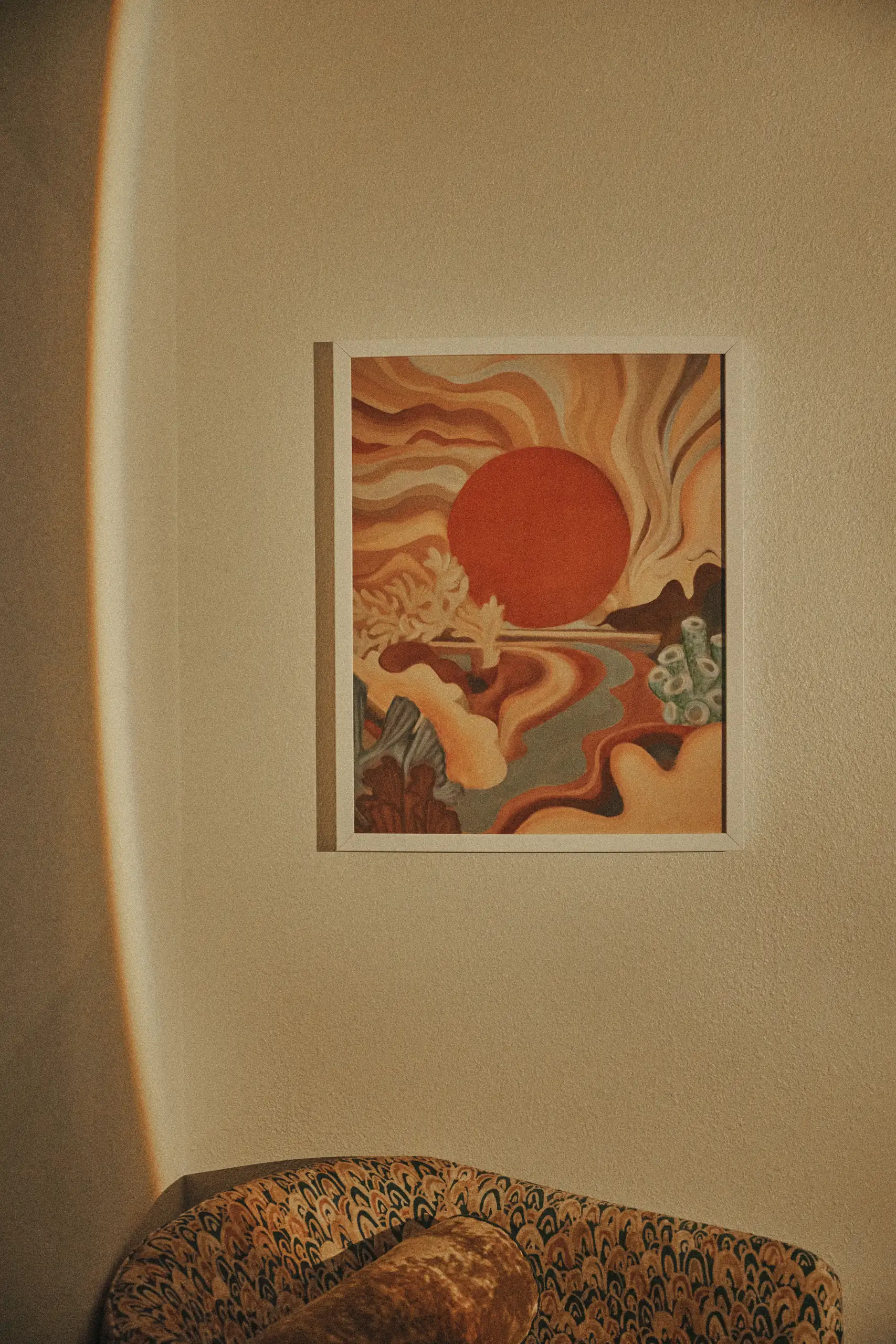 Abstract painting of a red sun and flowing shapes hung on a beige wall above patterned furniture.
