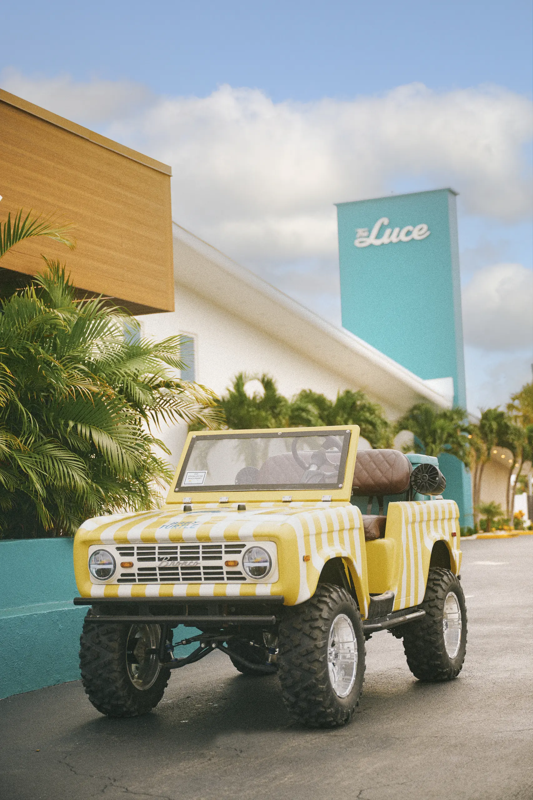 Yellow and white striped vintage-style off-road vehicle parked on a street near tropical plants.