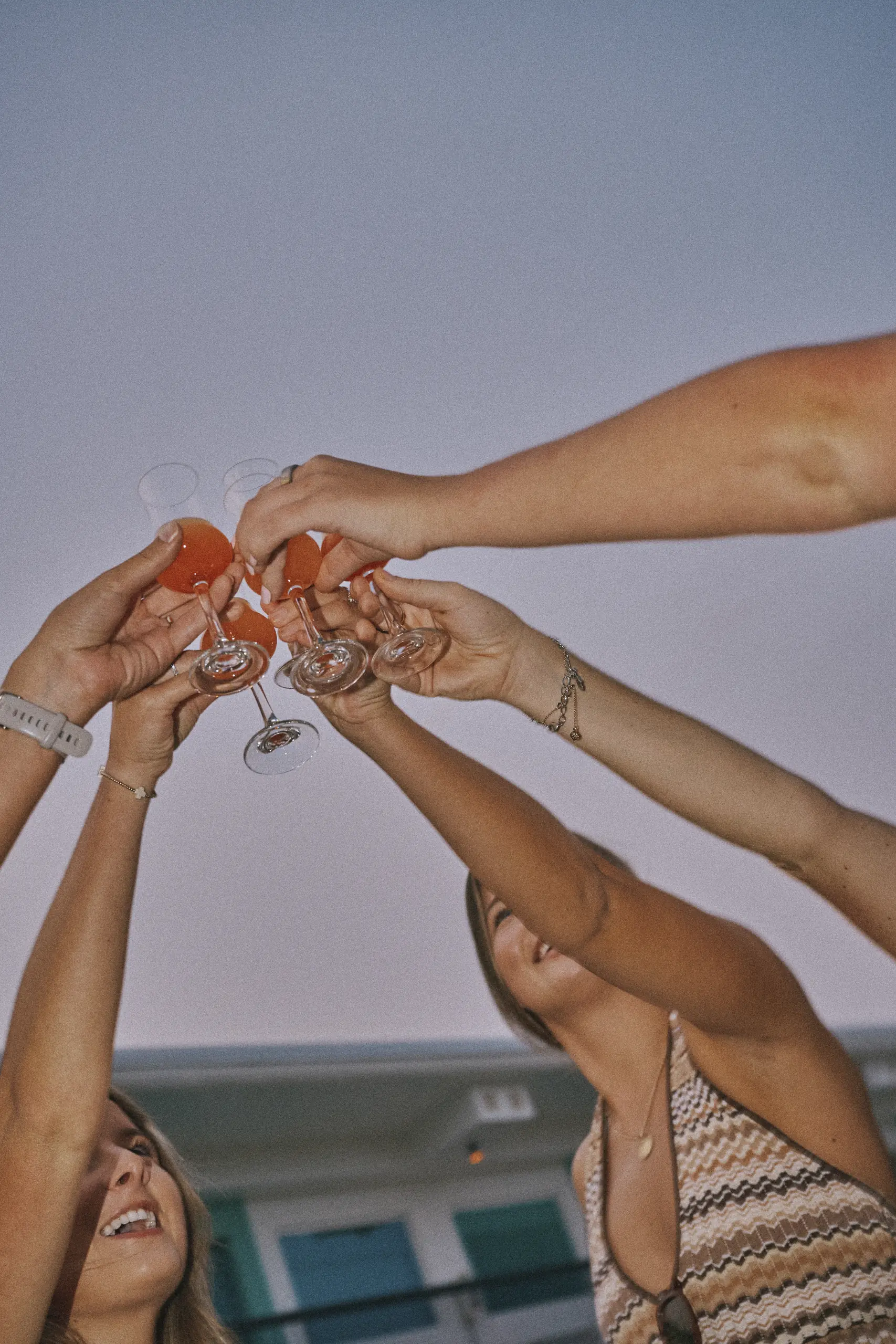 Group of friends raising glasses of orange drink in a celebratory toast outdoors at dusk.