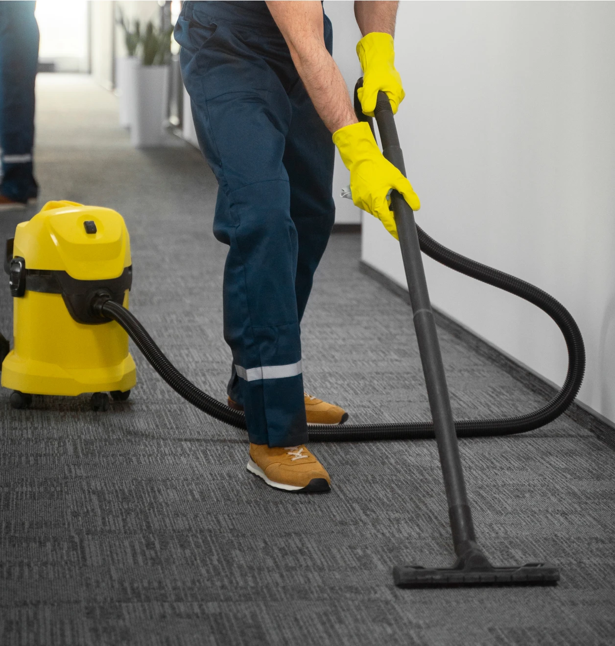 Cleaner using an industrial wet dry vacuum to remove dust from carpet in a commercial office corridor