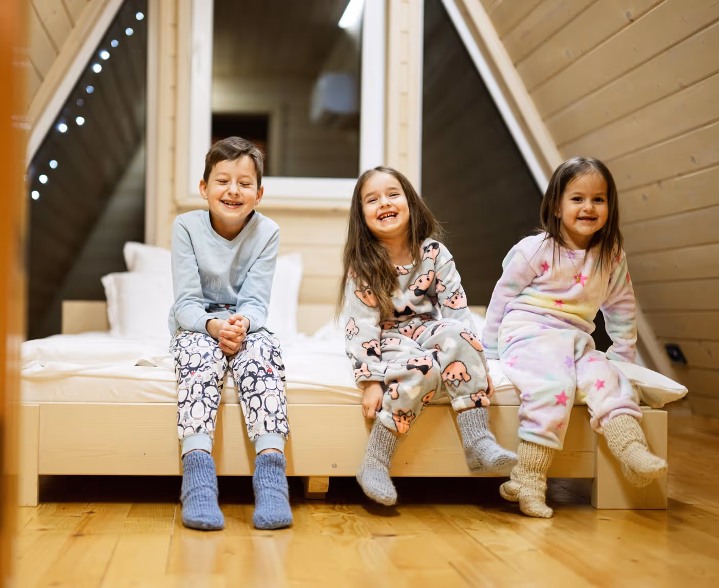 Three young children in pajamas sitting on a bed