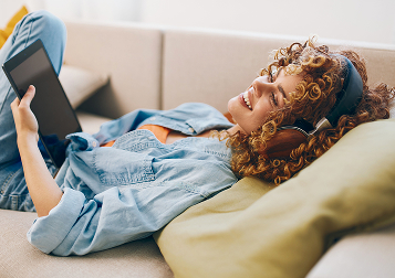 Woman with curly hair relaxing on a couch while browsing a tablet