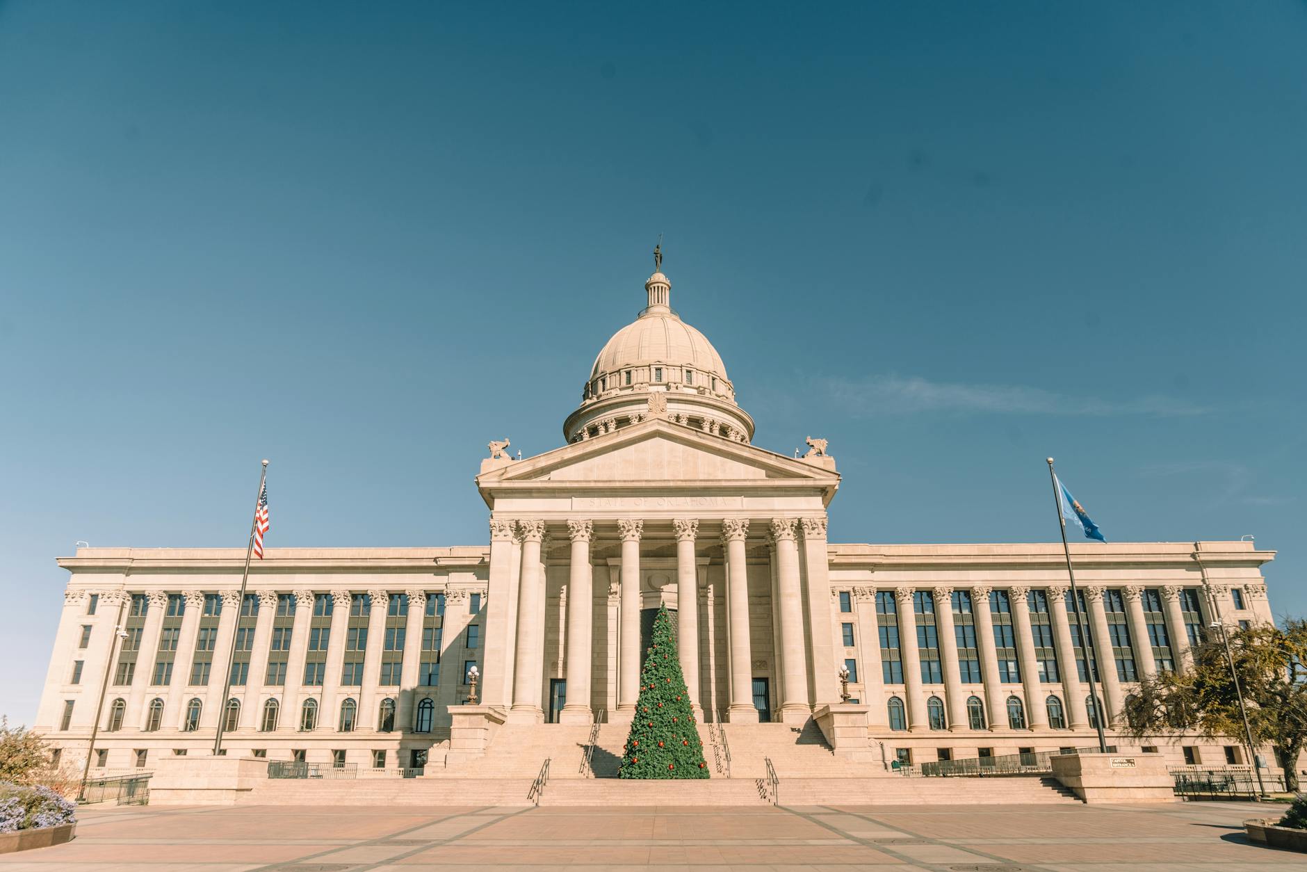 Front view of Oklahoma State Capitol adorned with a Christmas tree, under clear skies.