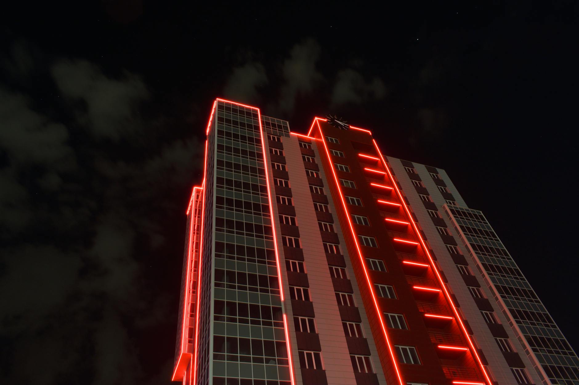 A striking view of a skyscraper with red neon lights against a night sky.