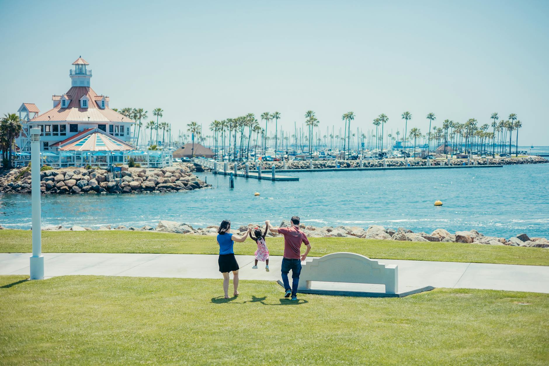 A family having fun by a marina with palm trees and a lighthouse, capturing a joyful moment.