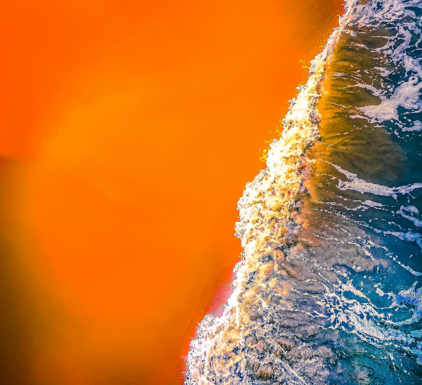 Dynamic aerial view of ocean waves meeting vibrant orange sand at Virginia Beach.