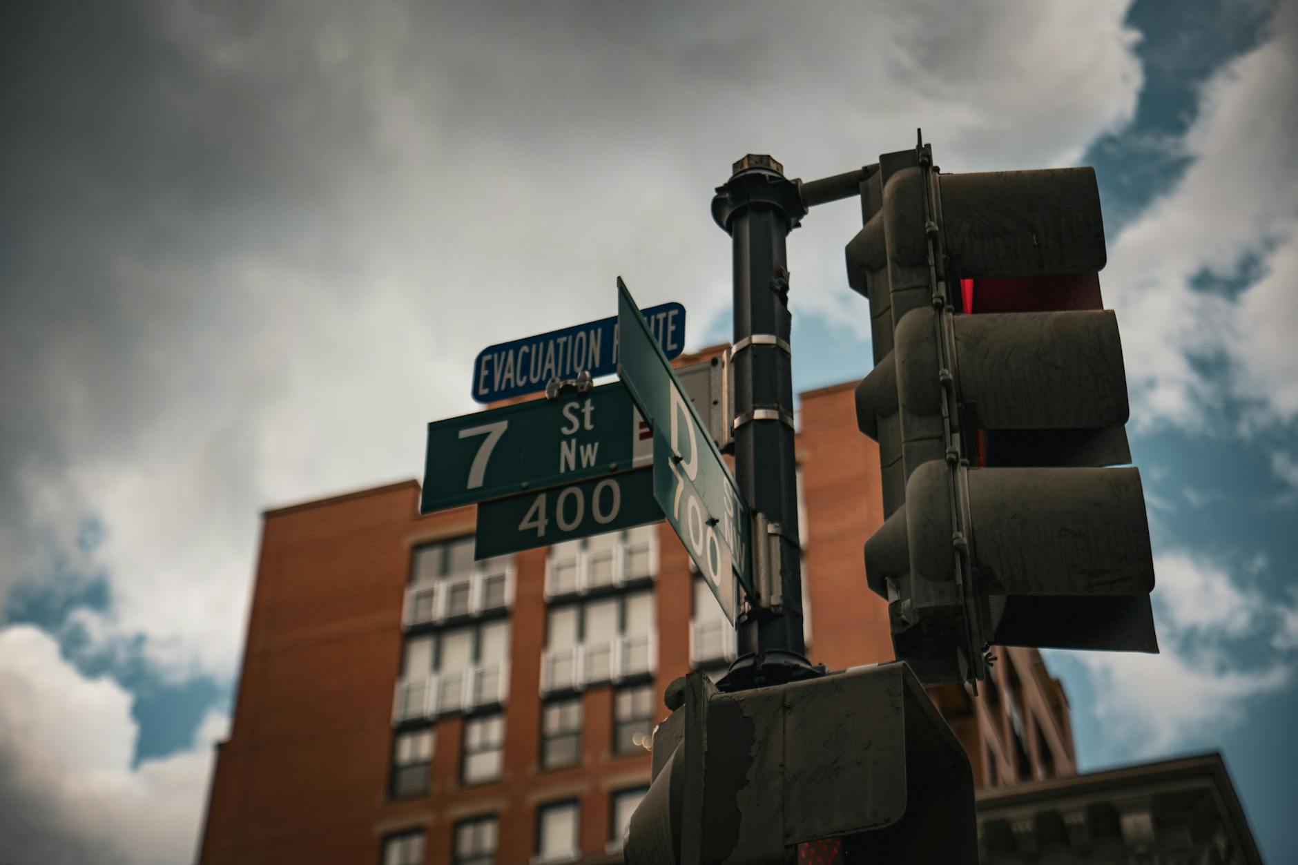 Street signs and traffic light at an urban intersection, cloudy sky.