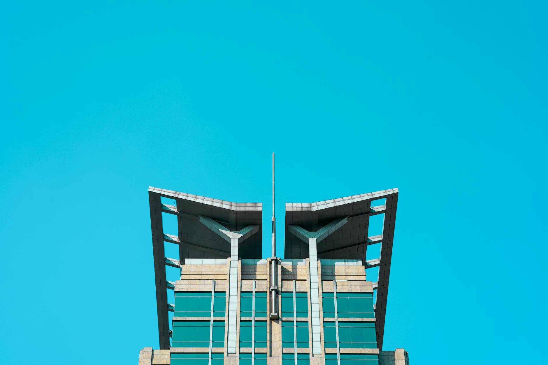 Top section of a modern high-rise building with unique design against a clear blue sky.