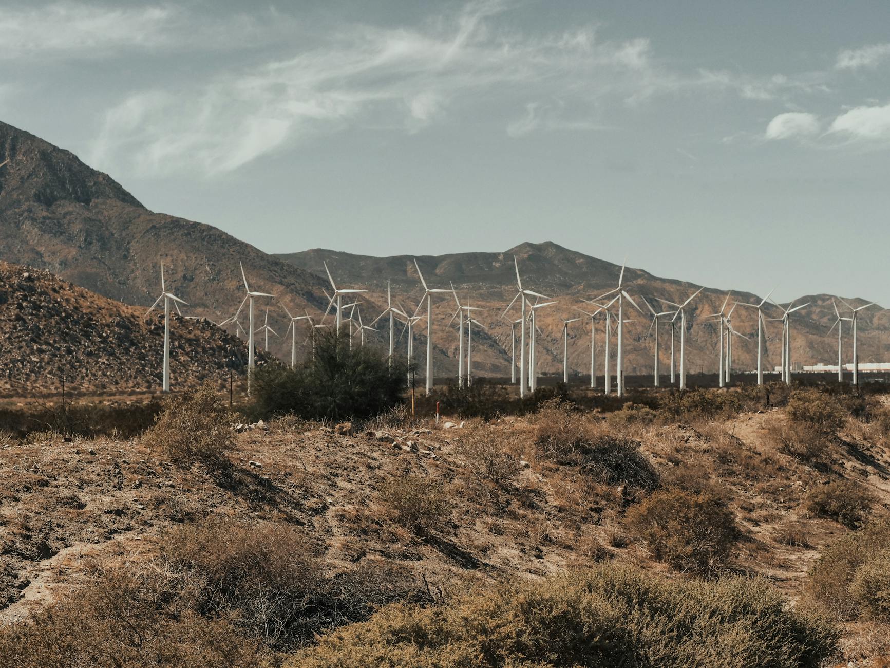 Wind turbines generating clean energy in a mountainous desert landscape under a clear sky.