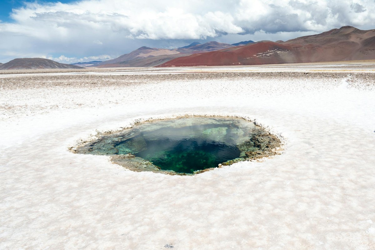 A stunning view of the Ojo de Agua at Salinas Grandes, Catamarca, with vibrant colors and majestic mountains.