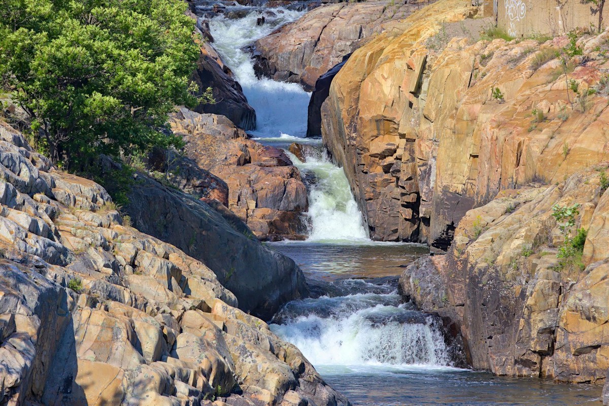 A tranquil waterfall flowing through rugged rock formations surrounded by lush greenery.