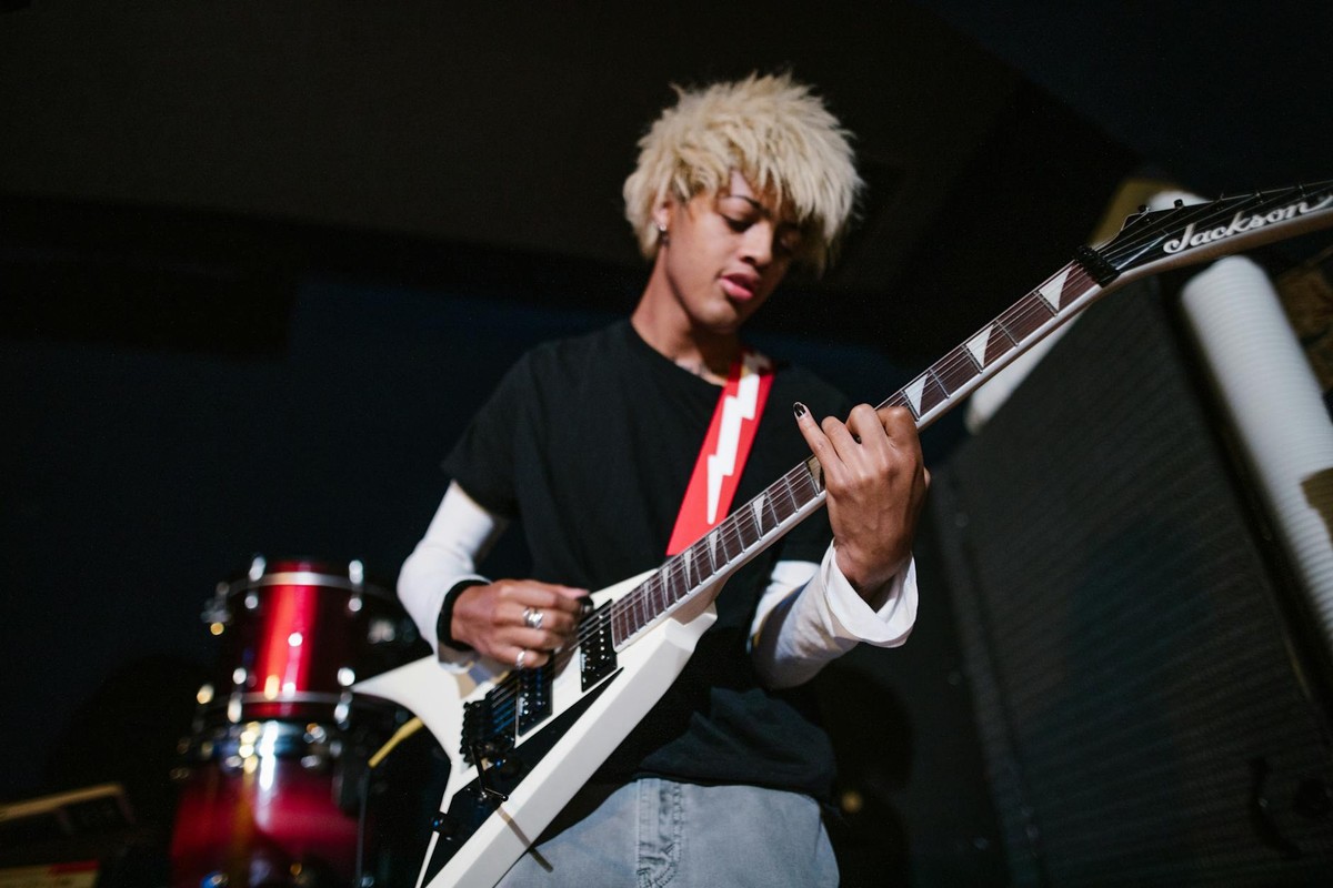 Energetic young guitarist playing a white electric guitar in a dimly lit room.