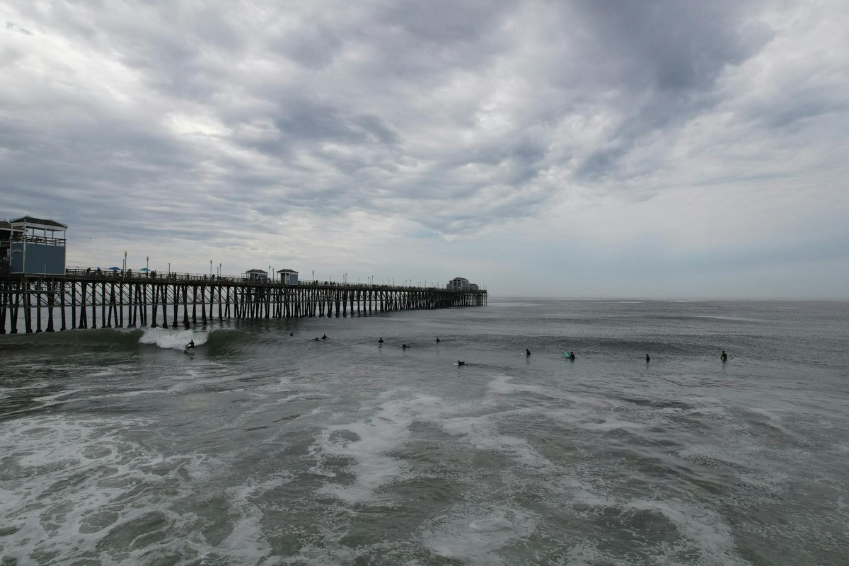 Surfers ride waves near Oceanside Pier, California under a moody sky.